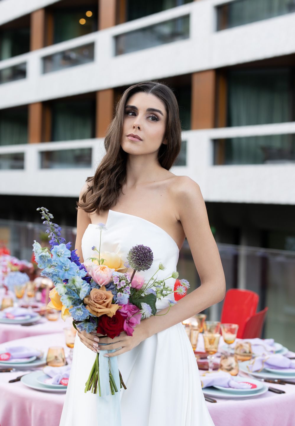 Vivienne Oesch posing as a bride in a white dress holding a colorful bouquet at the FIVE HOTEL ZURICH. Wedding makeup in Zurich. Hair and makeup by Denise Dedich.