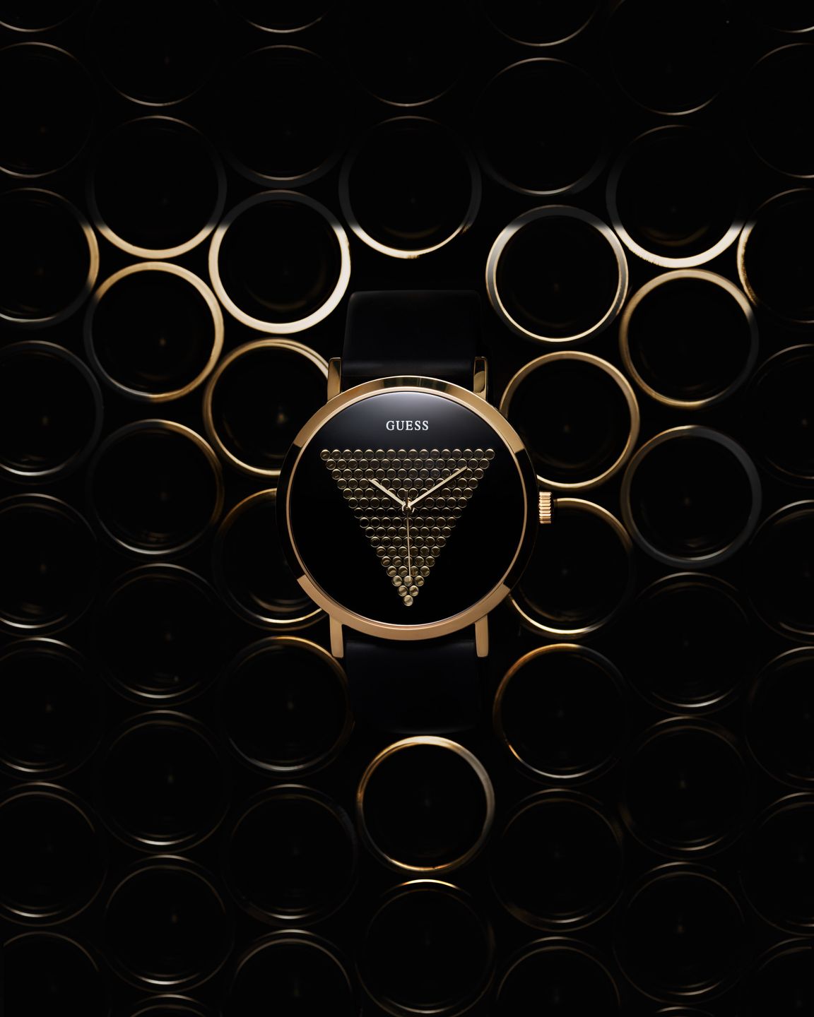 Guess watch with a gold-triangle motif, set against a backdrop of golden circular patterns and triangle-shaped lighting that mirrors the watch dial design.