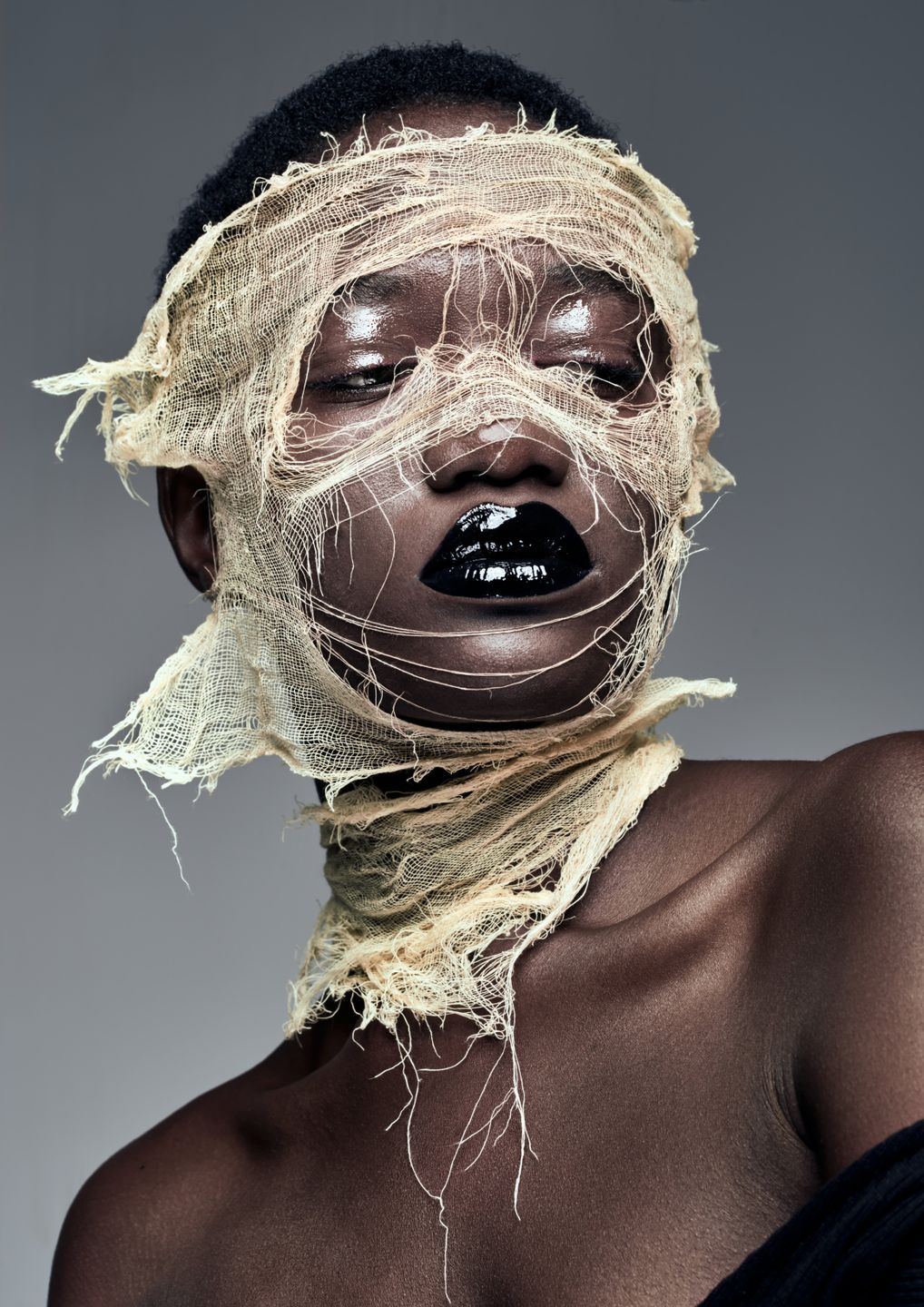 Model wrapped in gauze, with glossy black lips, creating an artistic representation of vulnerability and beauty