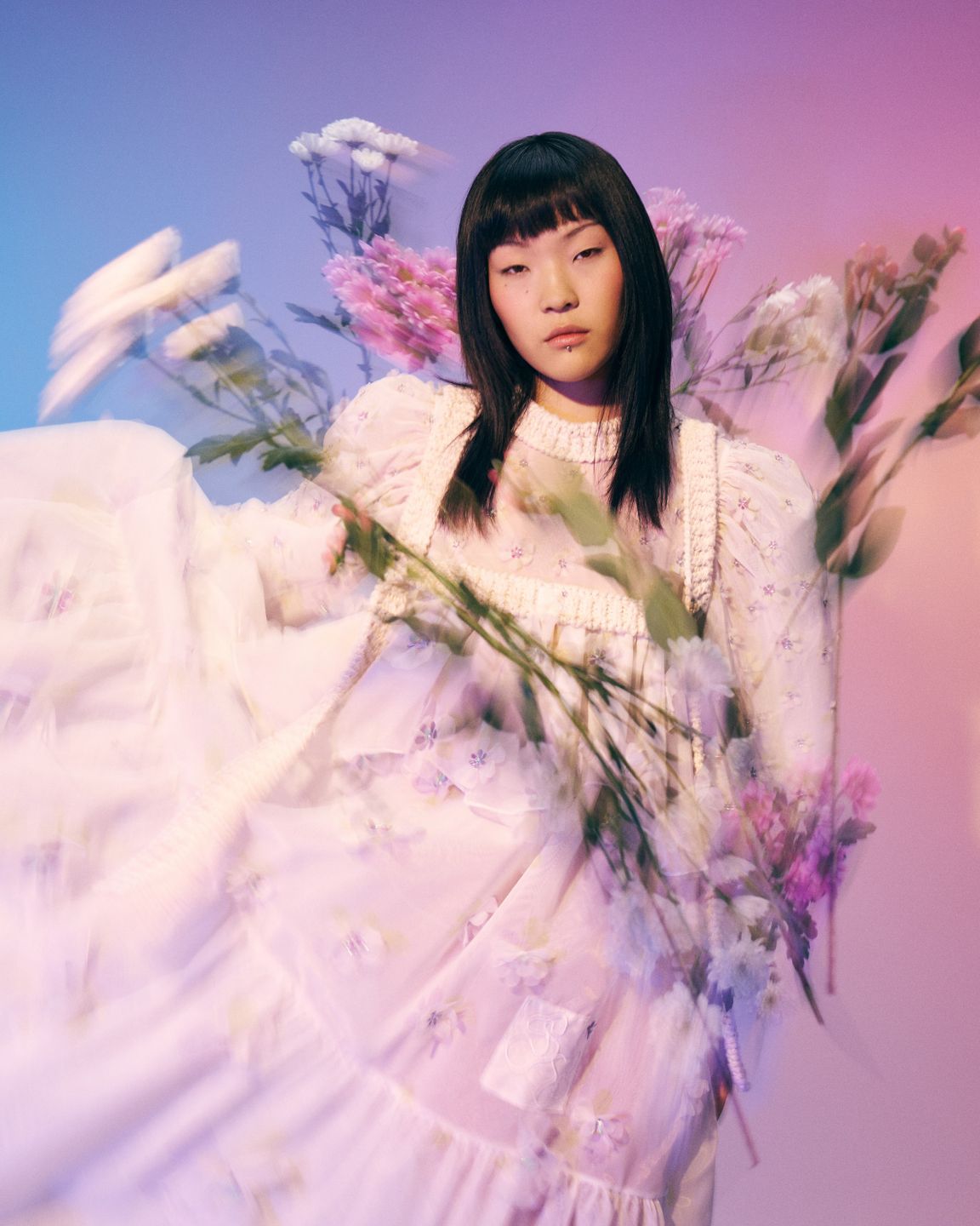 Model Anujin wears a Selina Rotach white dress, surrounded by flowers. Hair and makeup by Denise Dedich.