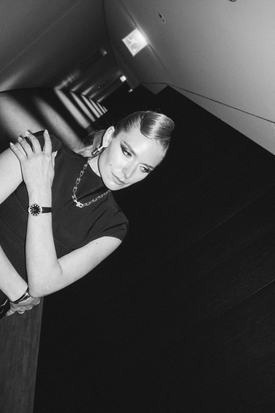 A black and white photo of model Jasmin Brunner, posing in a black Maison Alaia dress in The Dolder Grand Hotel during the Zurich Film Festival. She wears Tiffany earrings, necklace and watch. Her foundation is dewy, her eye makeup is smokey and glam. Makeup by Denise Dedich.