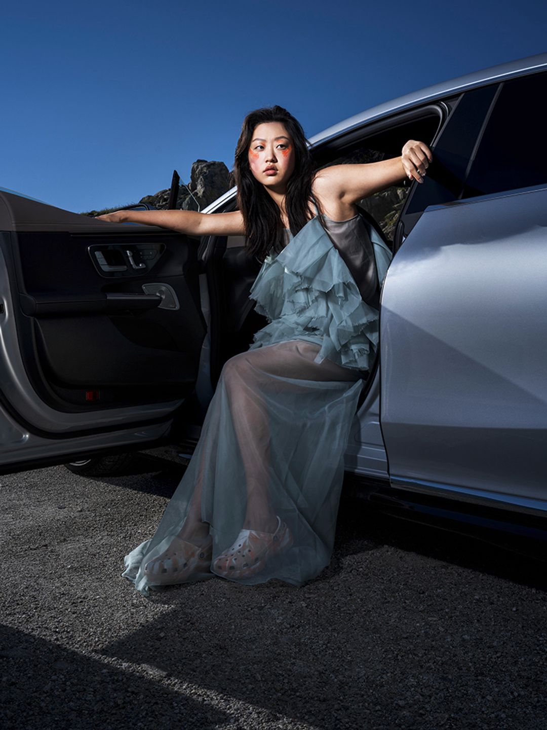 Model Dami J sits in a MERCEDES EQE. She has a bold orange eye makeup. Hair and makeup by Denise Dedich.