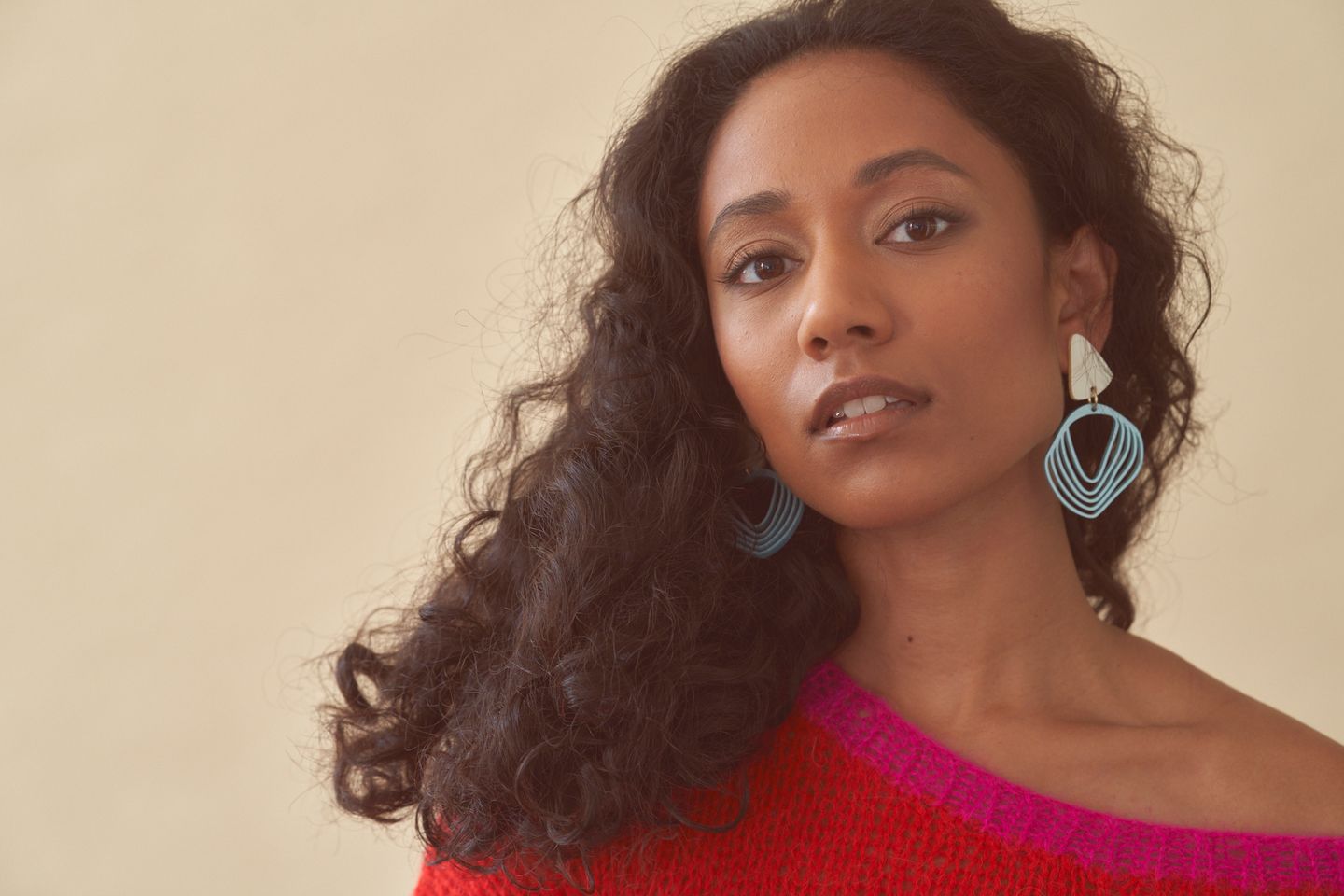 Model Devi Boddu wearing a pink and red sweater and blue Vanto earrings. Natural makeup. Hair and makeup by Denise Dedich.