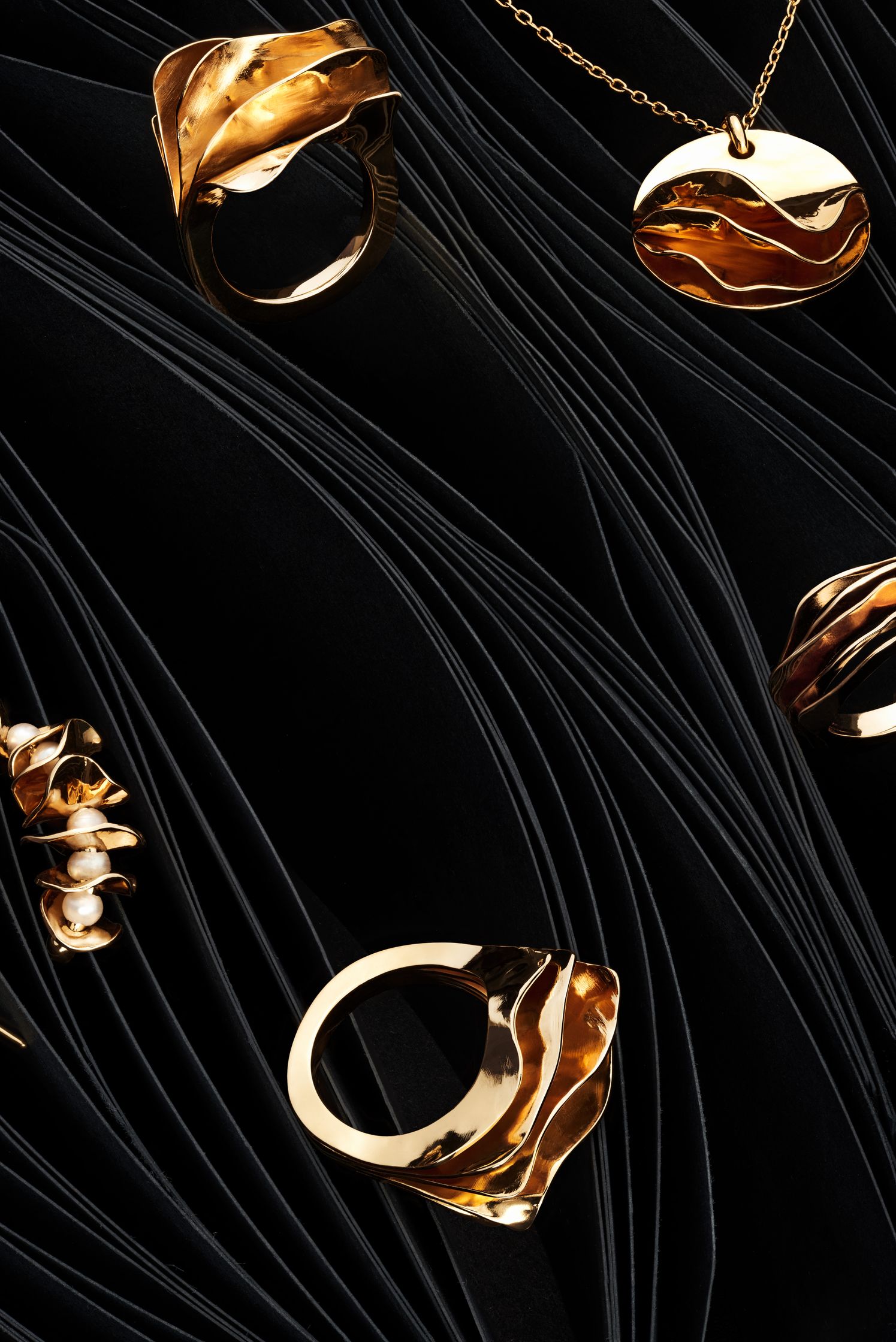 Collection of gold jewelry by Lisa Motte arranged on black paper waves, emphasizing the natural elegance of the designs.