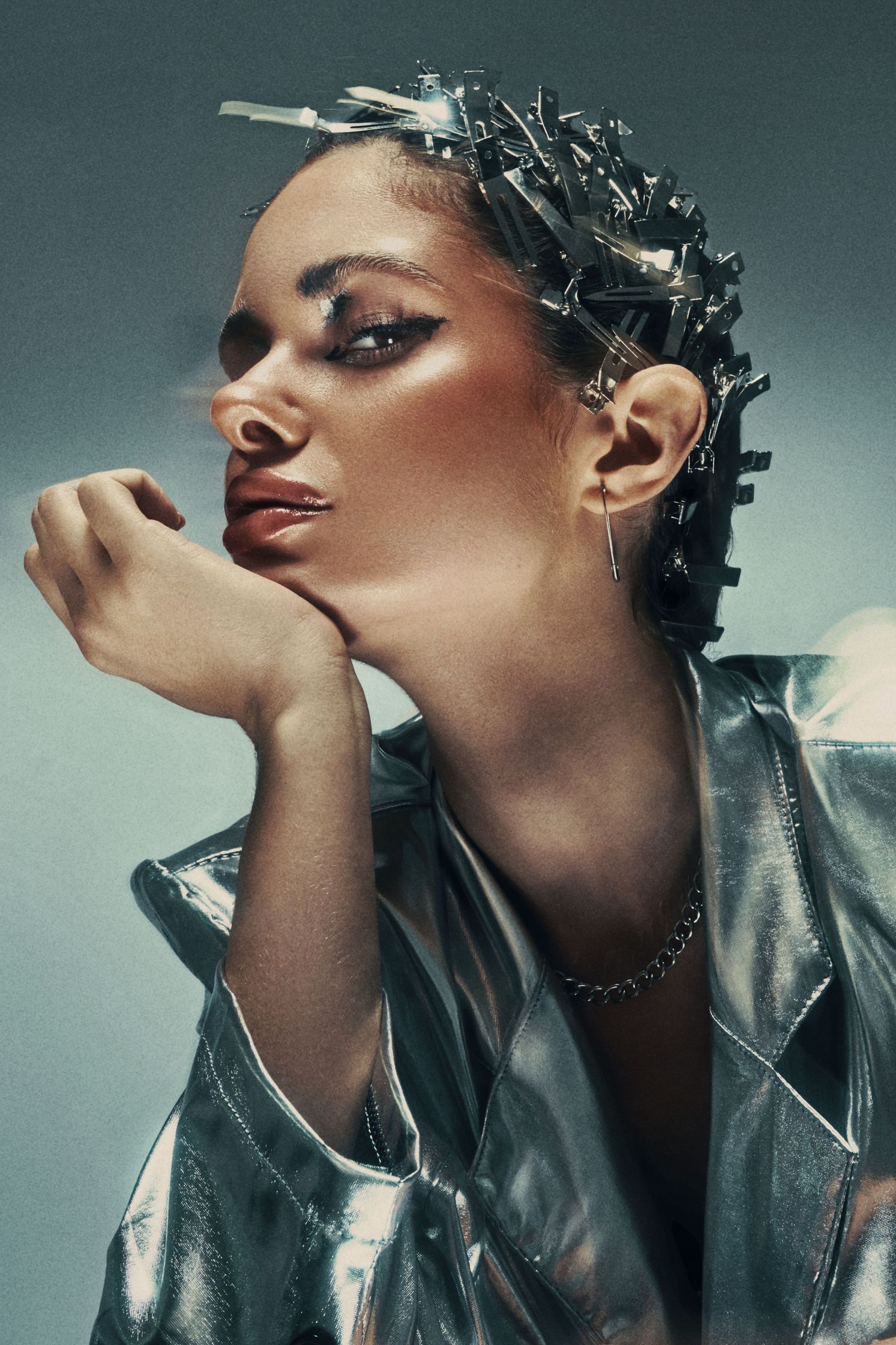 Close-up portrait of Monique Bourscheid in a silver metallic jacket with intricate hair clips and bold makeup.