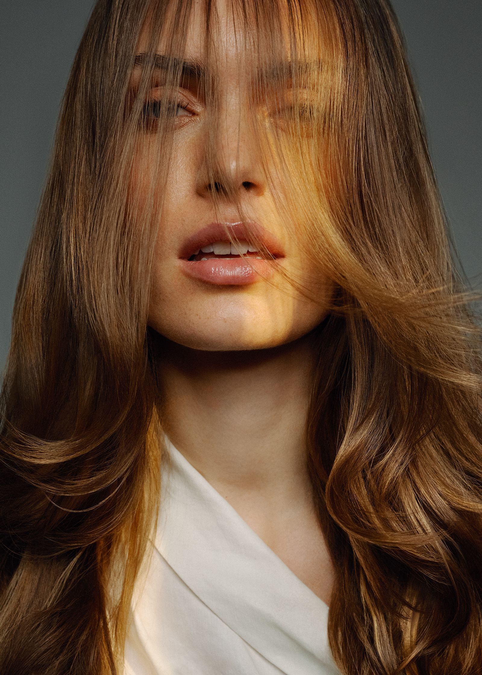 a woman with long brown hair is posing in front of a gray background