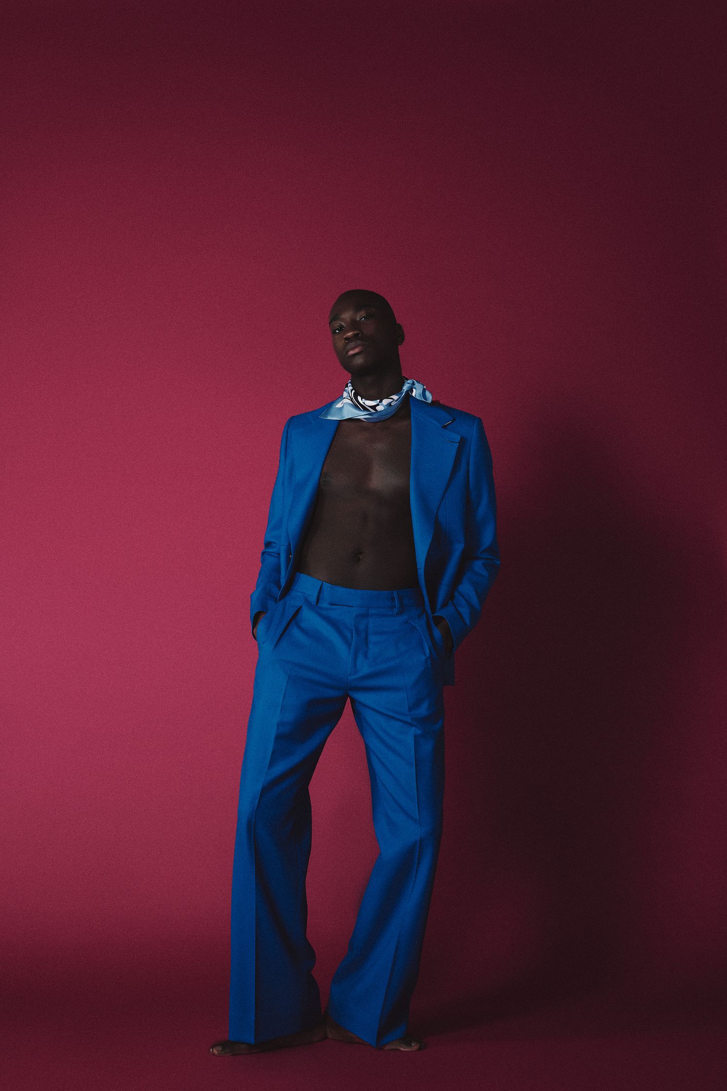 a man in a blue suit posing in front of a pink background