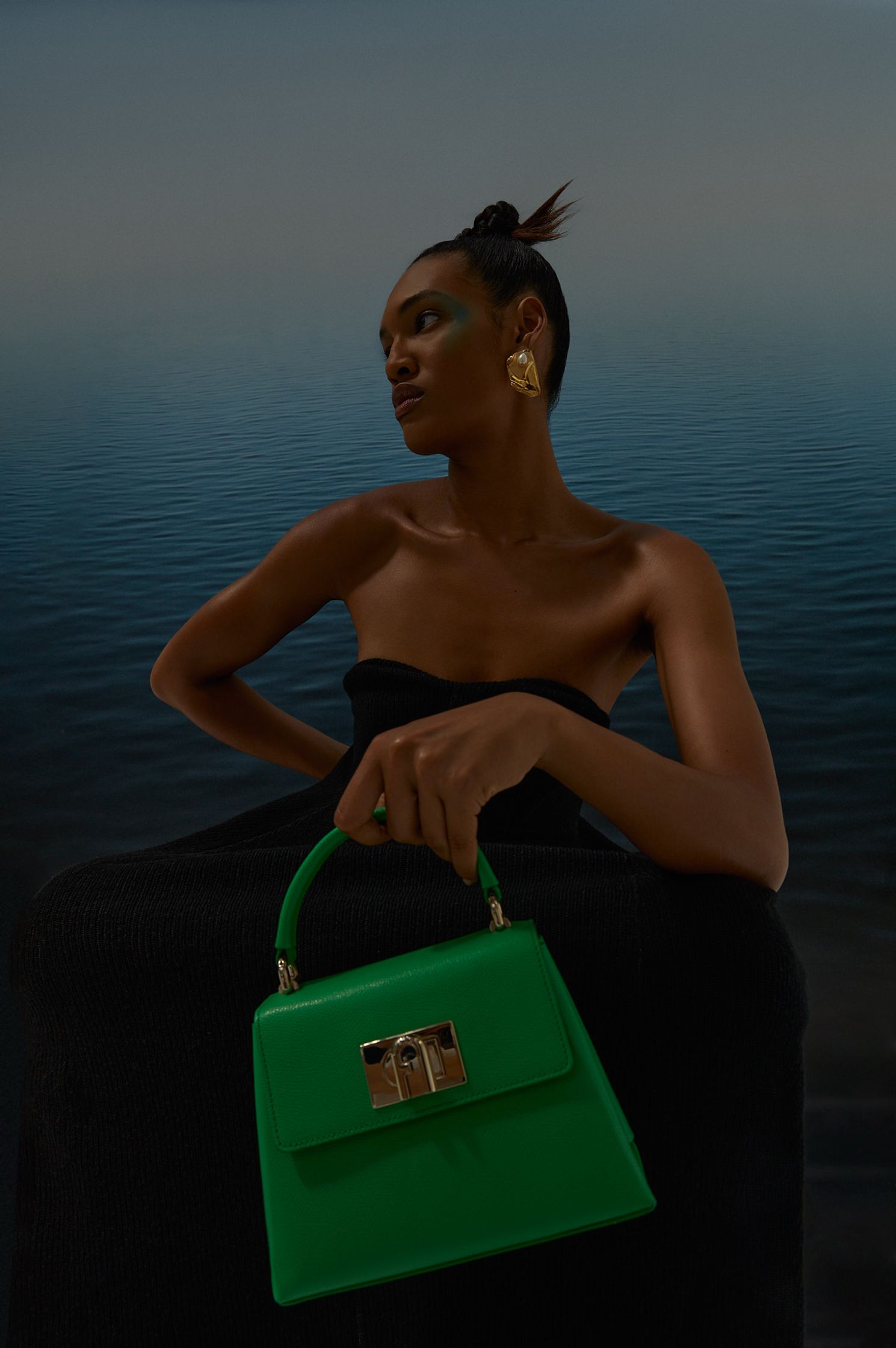 a woman holding a green handbag in front of a body of water