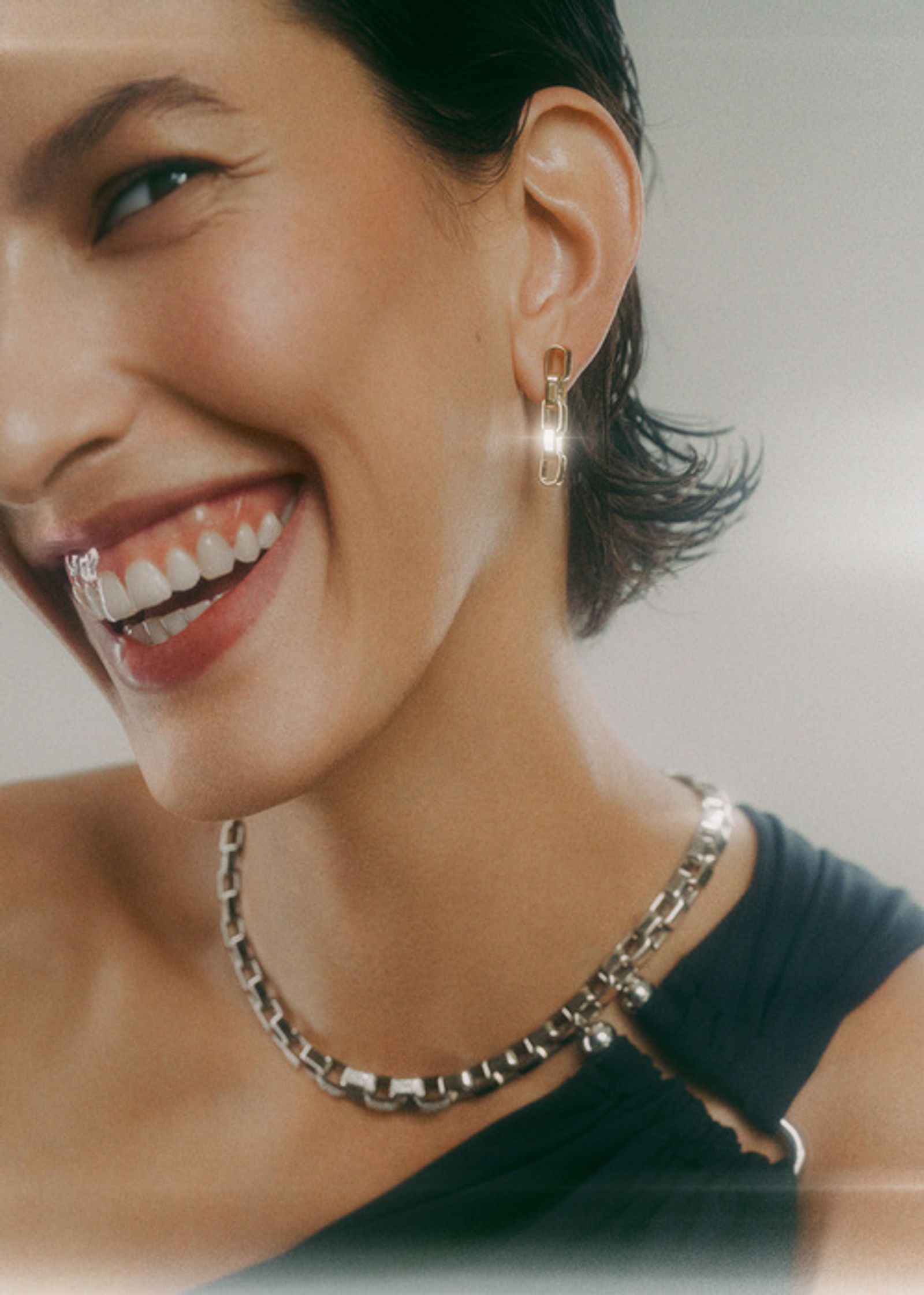 a smiling woman wearing a necklace and earrings