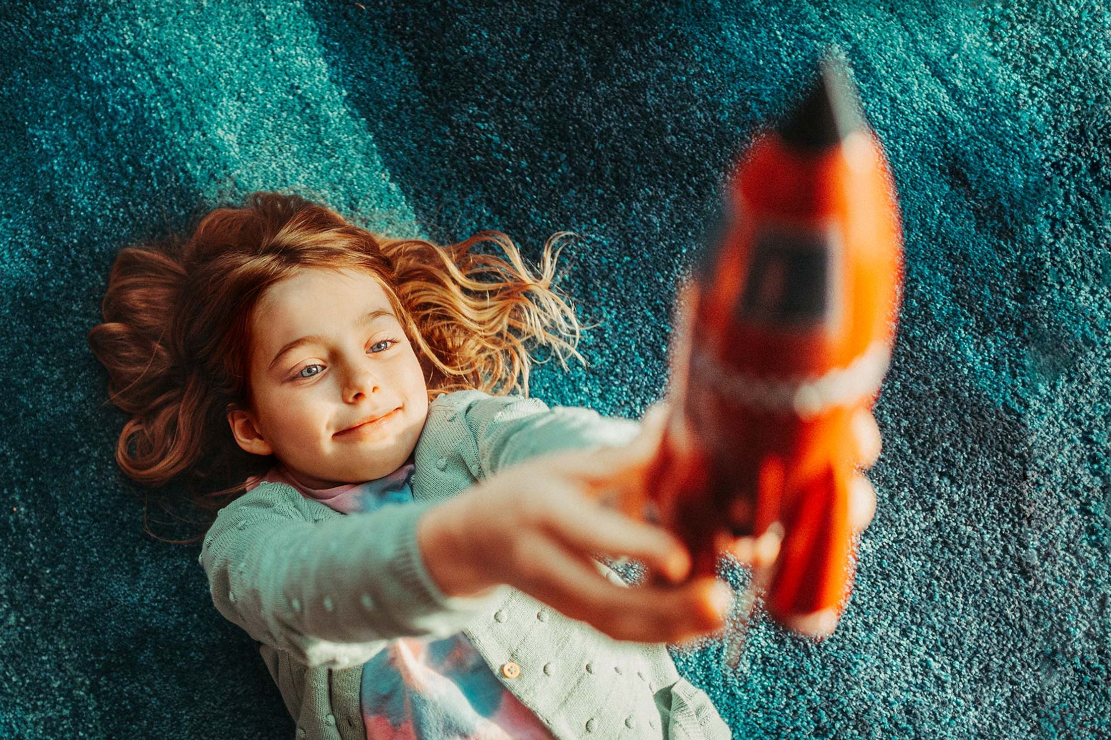 a girl laying on a rug with a toy rocket