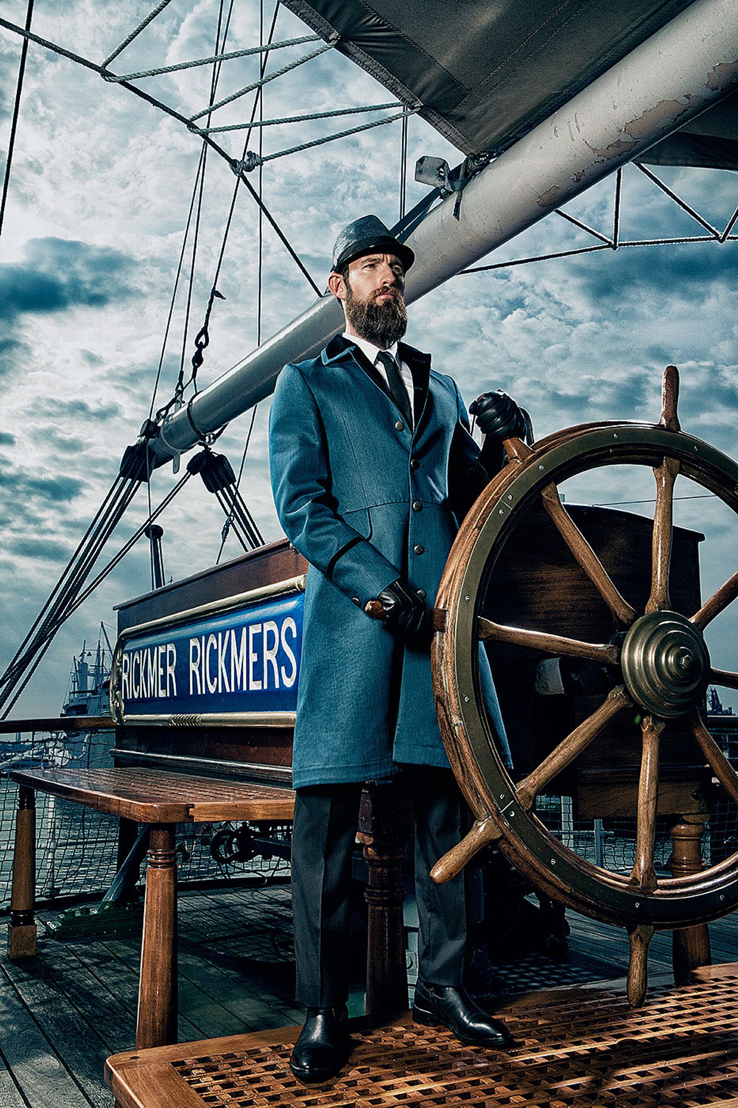 a man in a blue coat standing next to a ship's wheel Creative Retouching Hamburg