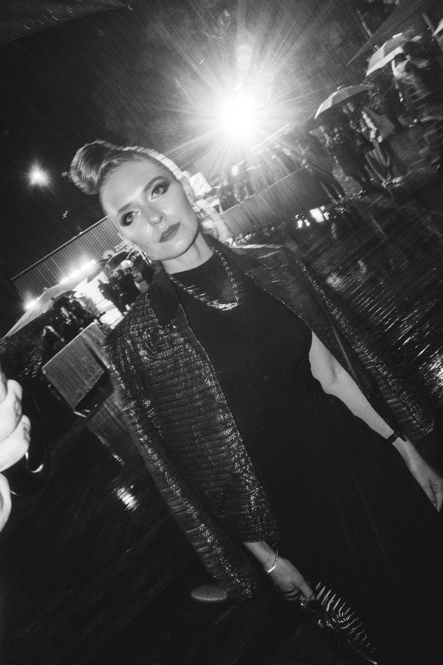 A black and white photo of model Jasmin Brunner, posing in a black Maison Alaia dress at the Zurich Film Festival. She wears Tiffany earrings, necklace and watch. Her foundation is dewy, her eye makeup is smokey and glam. Makeup by Denise Dedich.