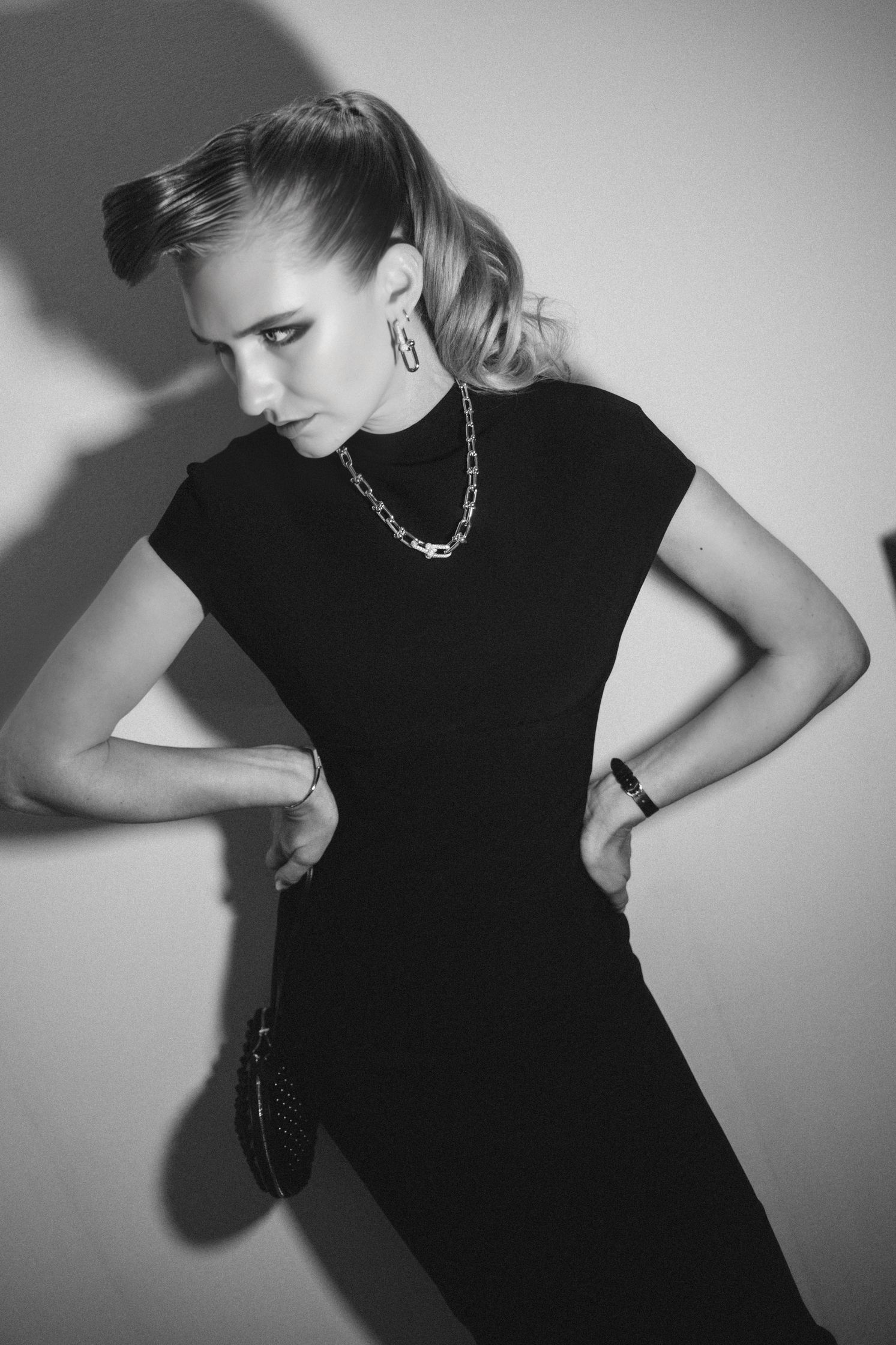 A black and white photo of model Jasmin Brunner, posing in a black Maison Alaia dress. She wears Tiffany earrings, necklace and watch. Her foundation is dewy, her eye makeup is smokey and glam. Makeup by Denise Dedich.