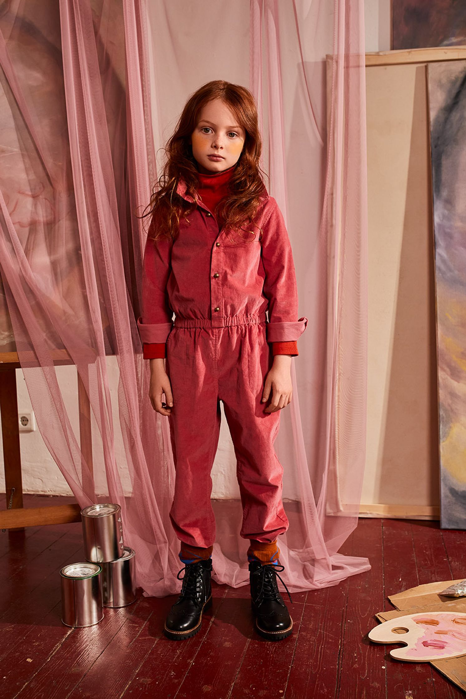 a girl in a red jumpsuit standing in front of a painting