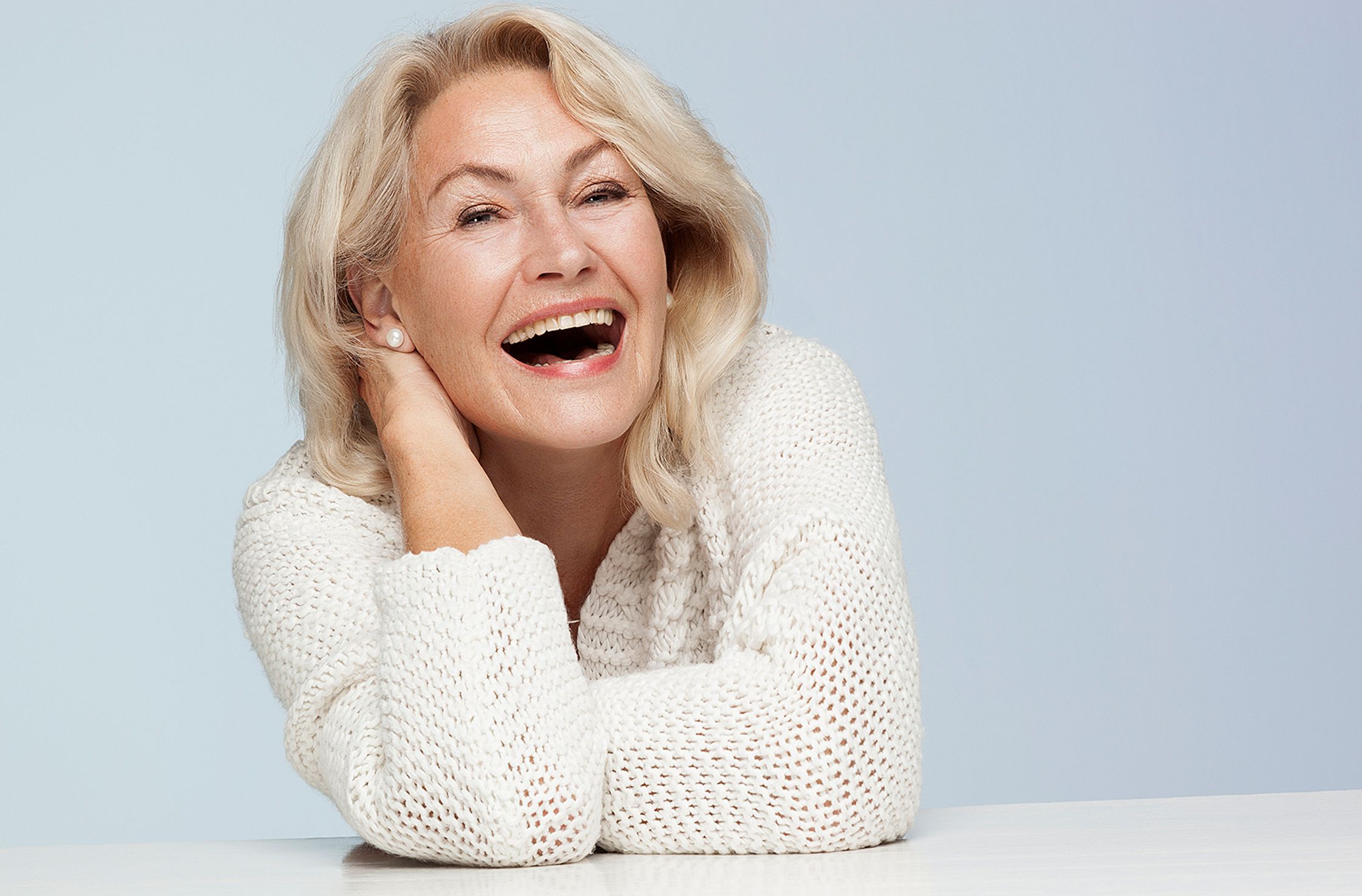 a woman is laughing while leaning against a table best ager post production