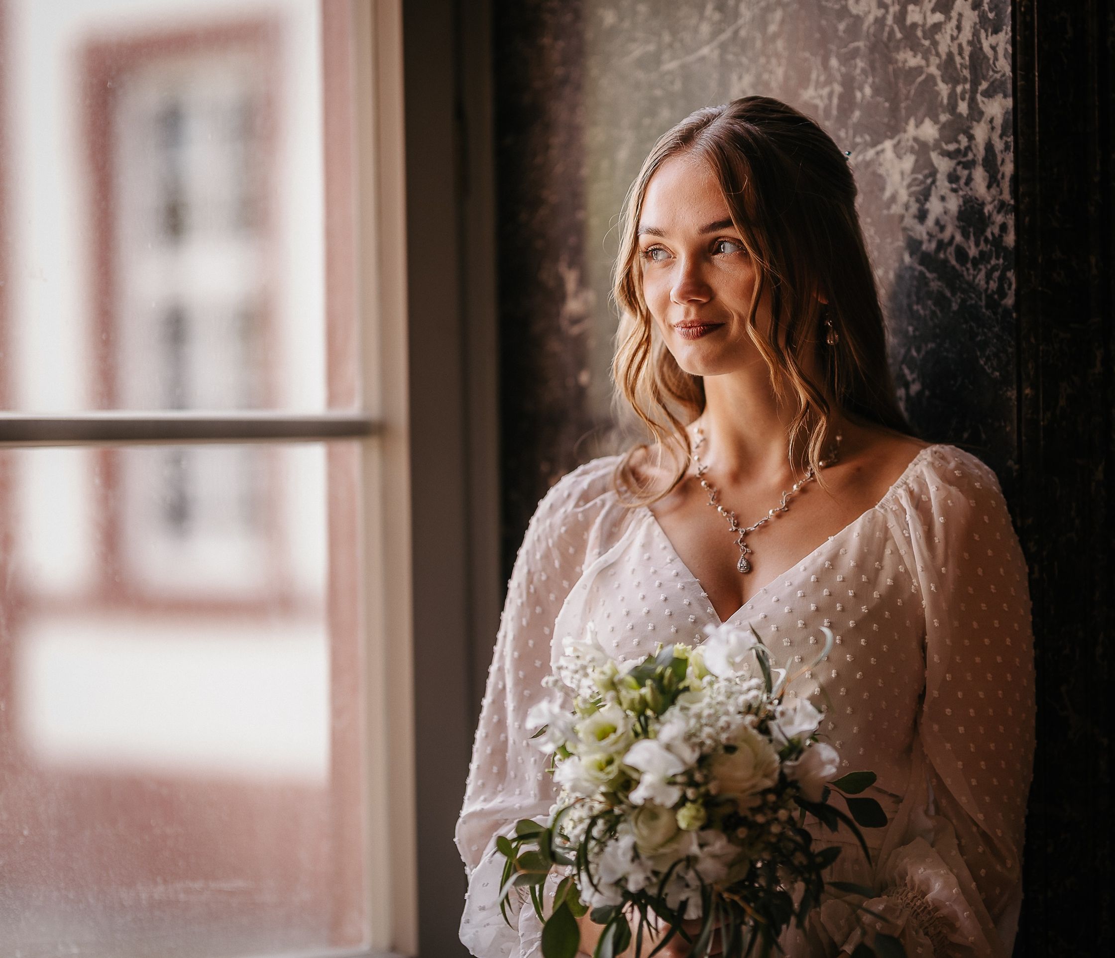 eine Braut in einem weißen Kleid, die an einem Fenster in schloss philippsruhe in hanau sitzt