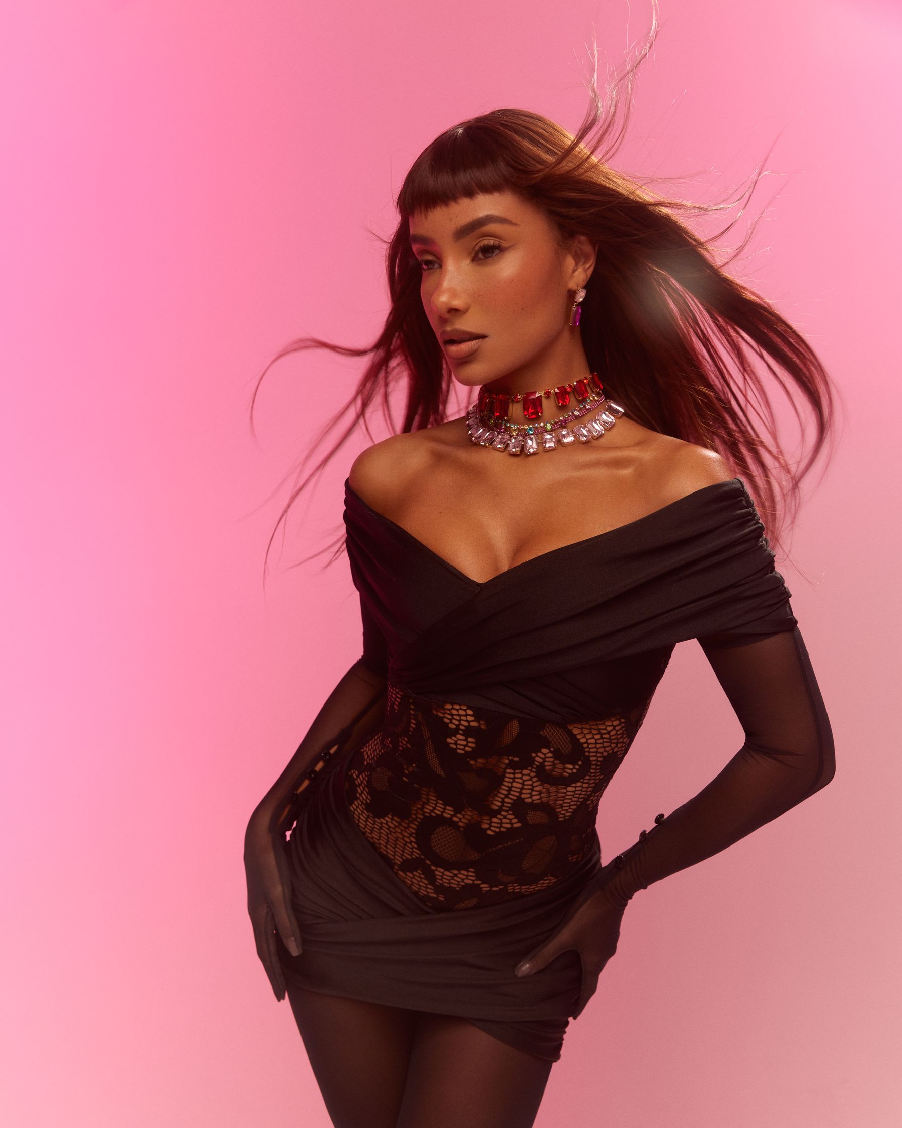 a woman in a black dress posing on a pink background
