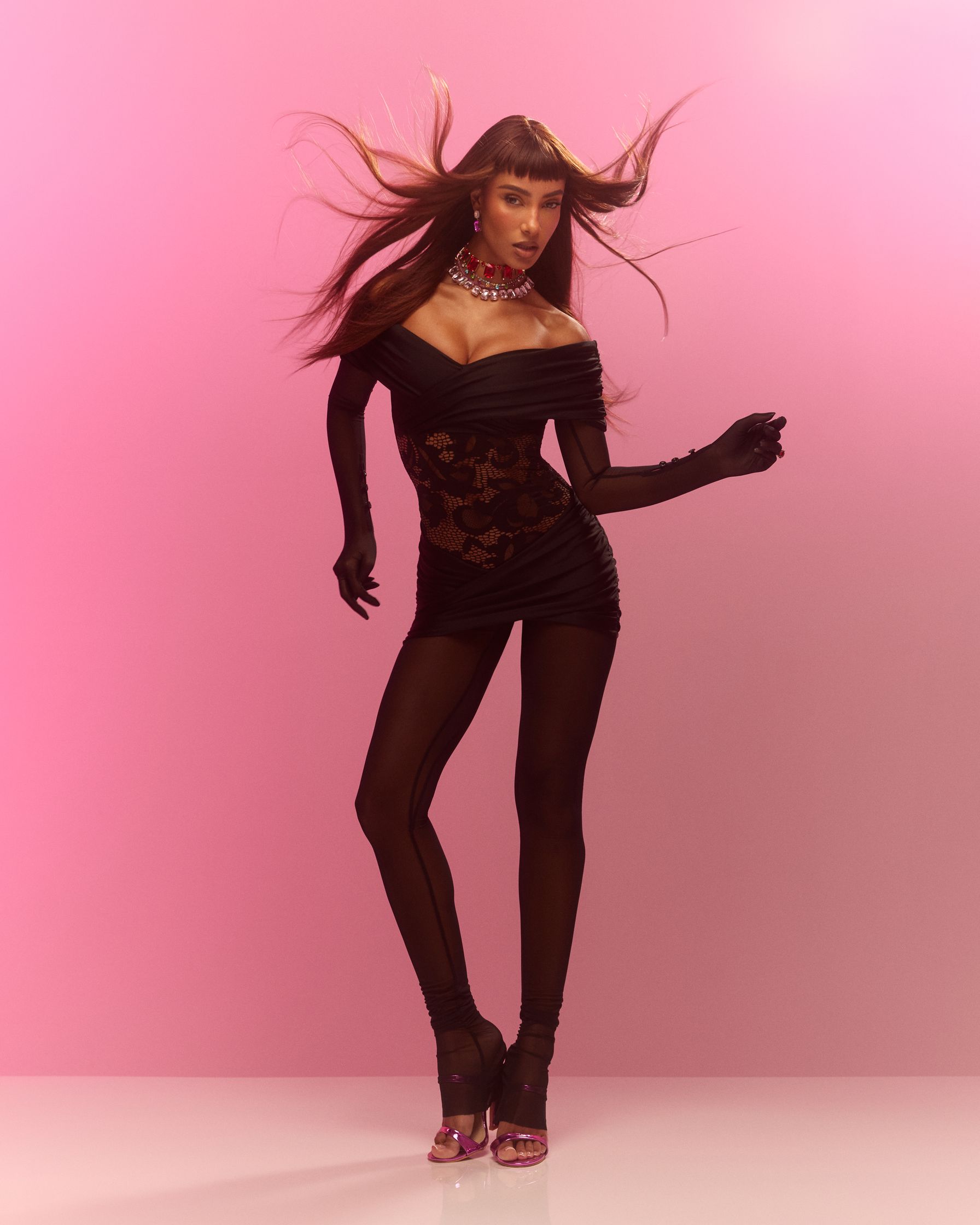 a woman in a black dress posing on a pink background