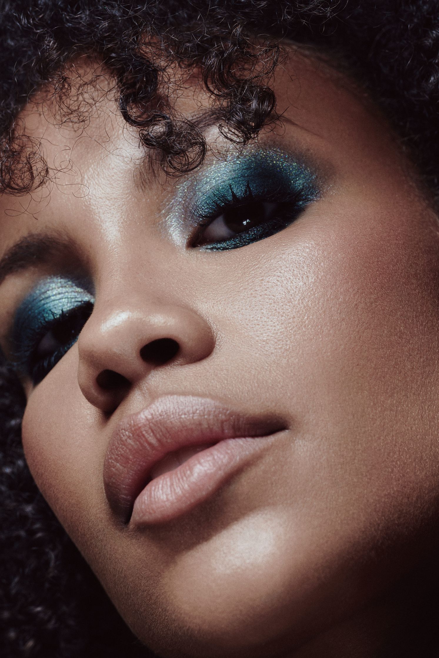 Close-up of Muriel Diem’s face, showcasing teal and metallic eye makeup with soft curls framing her face.