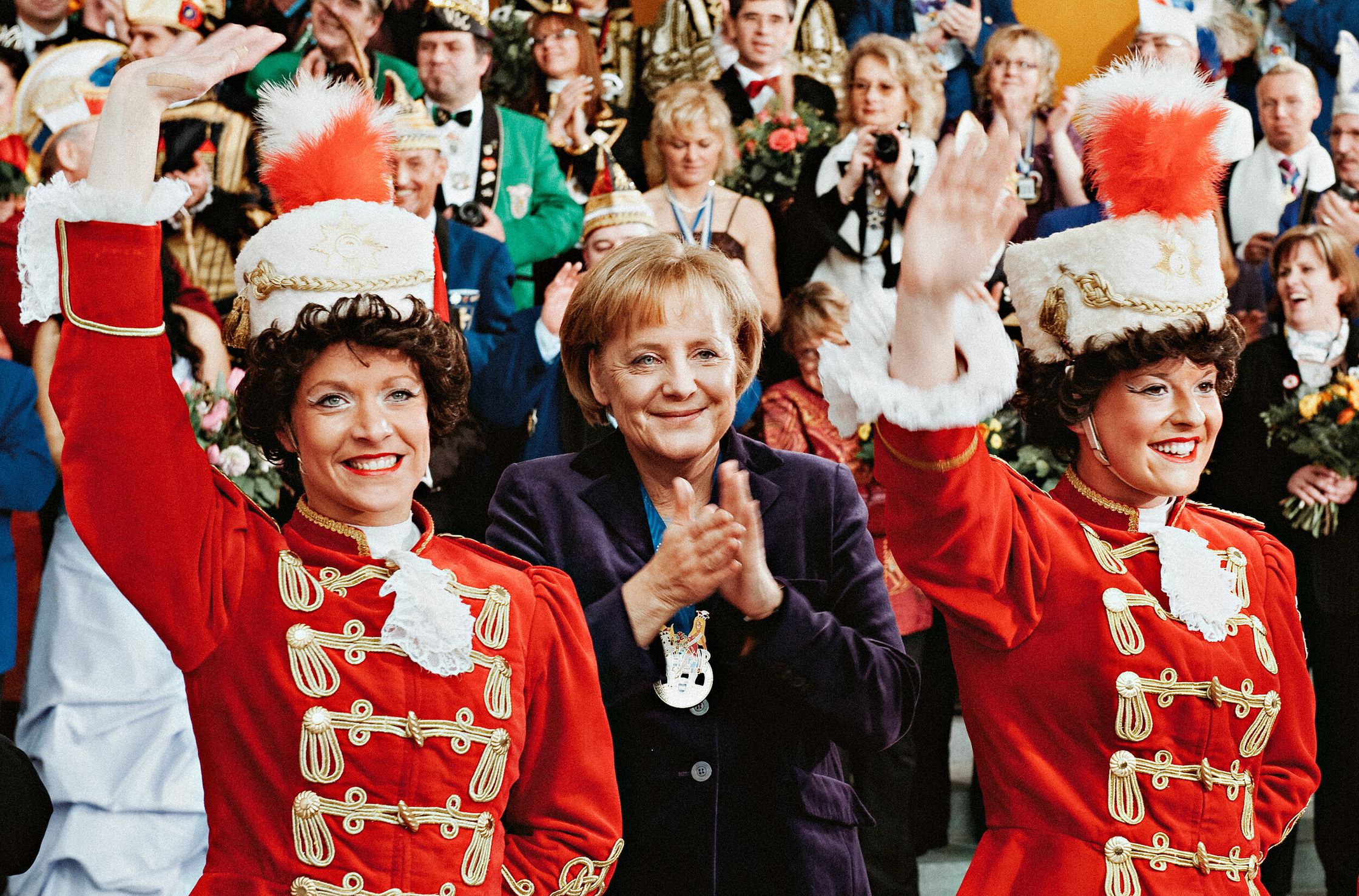 a group of women in red uniforms waving to the crowd angela merkel