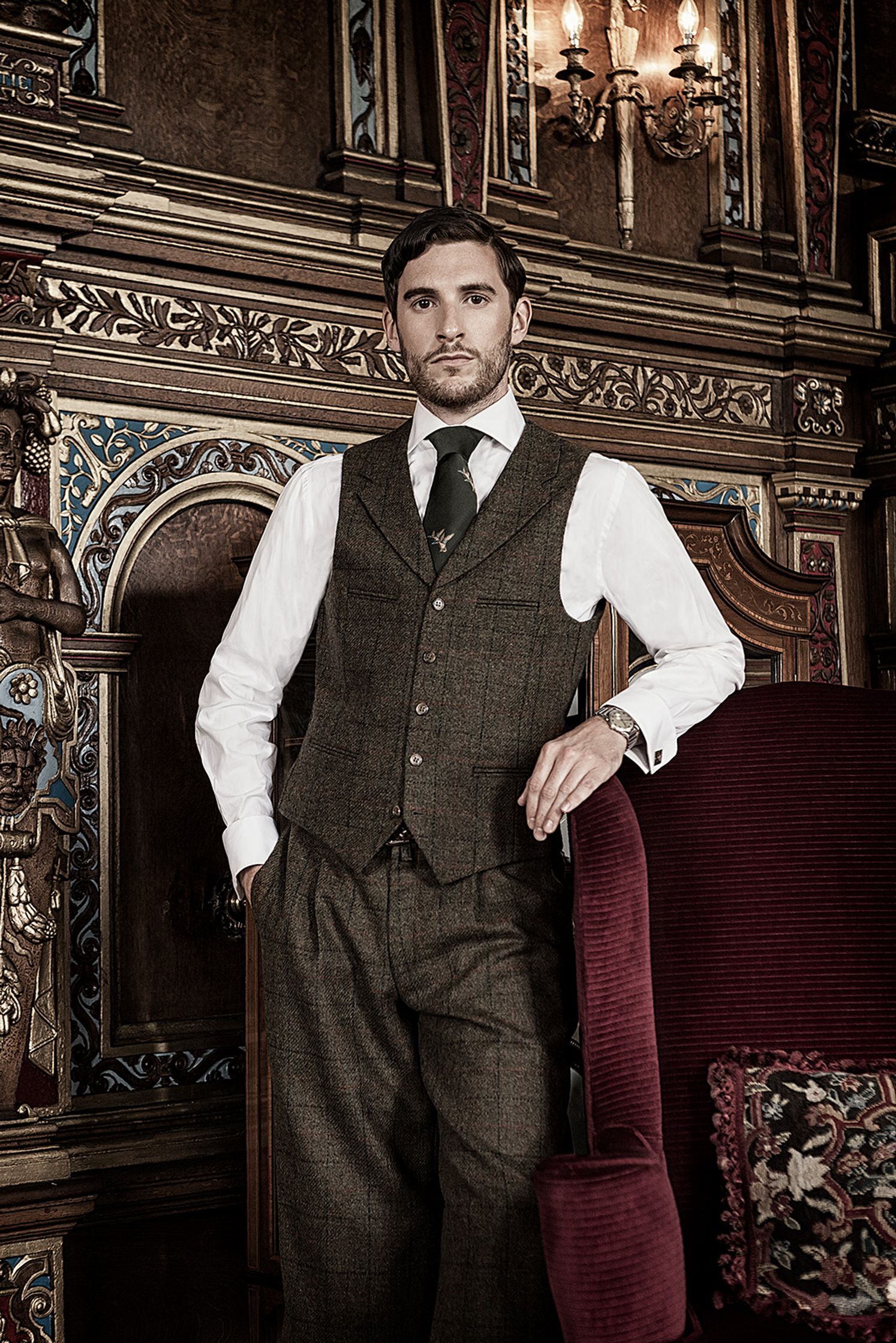 a man in a suit and tie is posing in front of an ornate chair creative post production