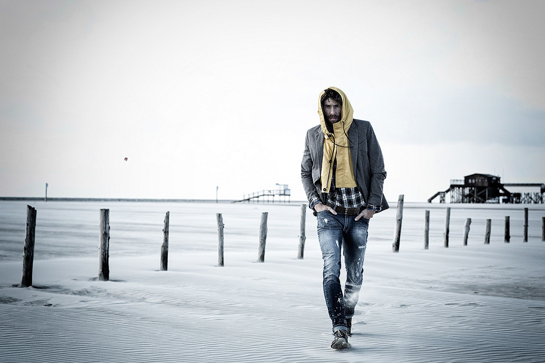 a man in a yellow hoodie walking on the beach post production image campaign