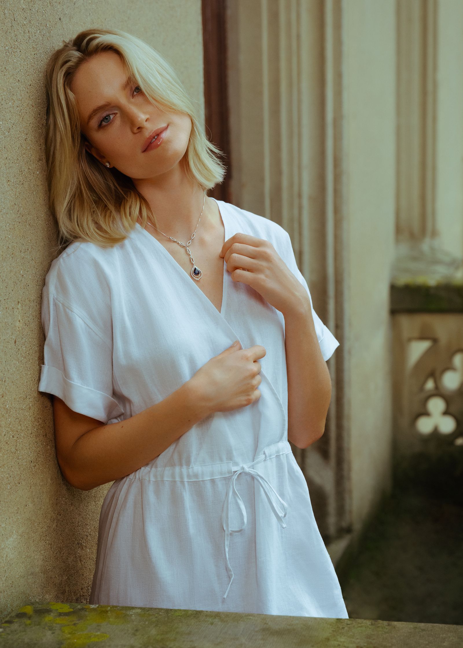 a woman in a white dress leaning against a wall