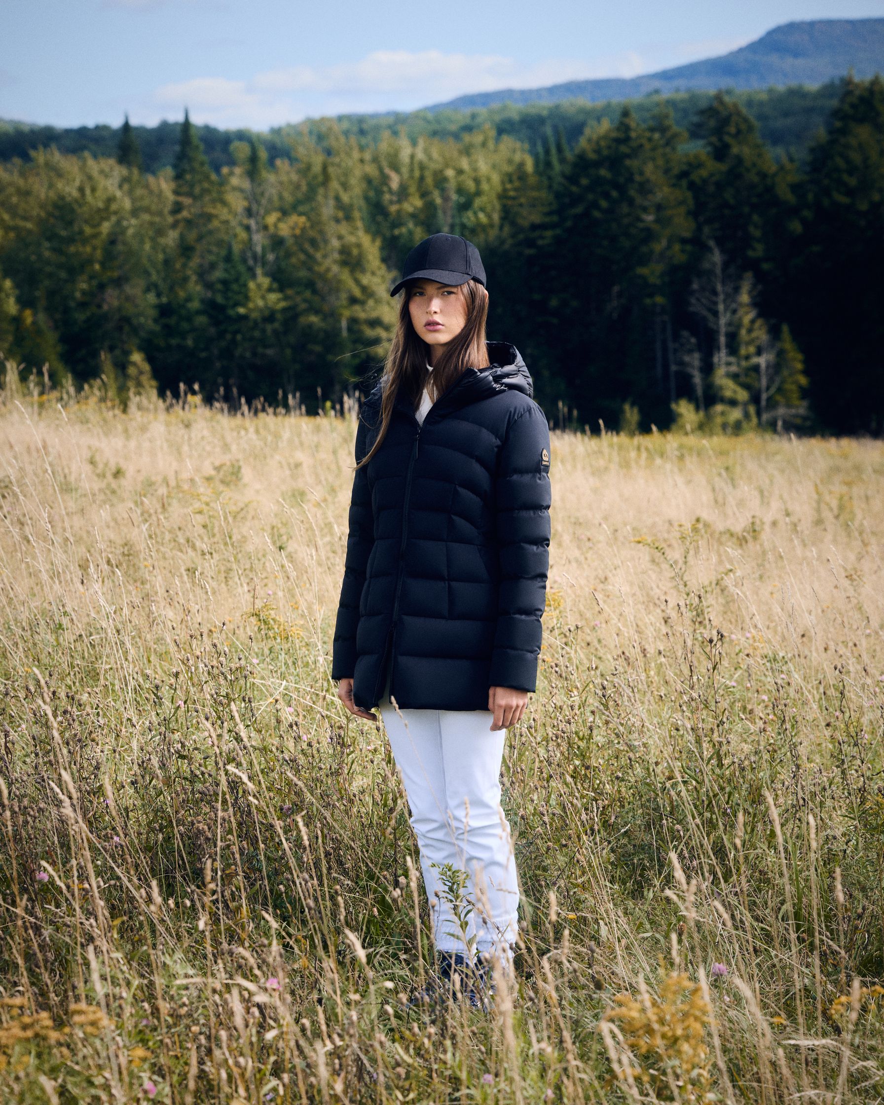 a woman in a black puffer jacket standing in a field