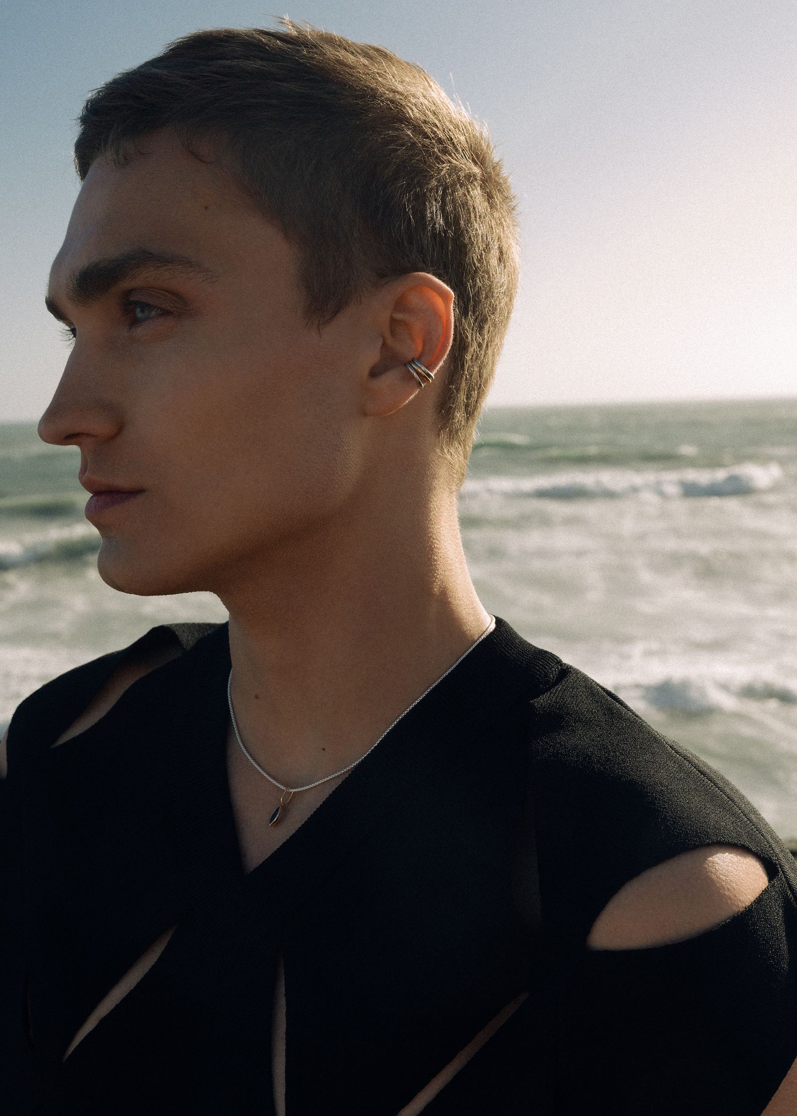 a young man standing by the ocean with a pierced ear