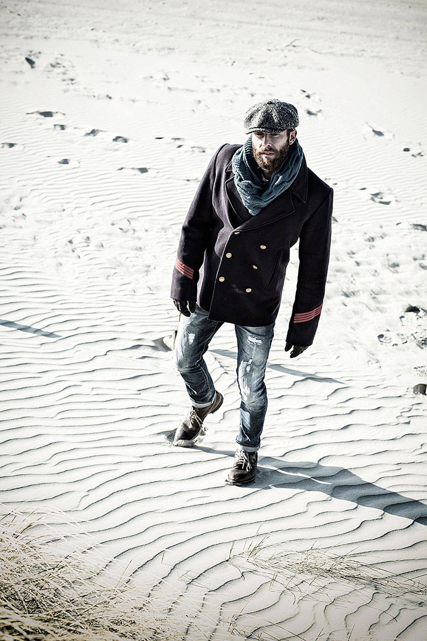 a man wearing a hat and jacket on the beach post production image campaign