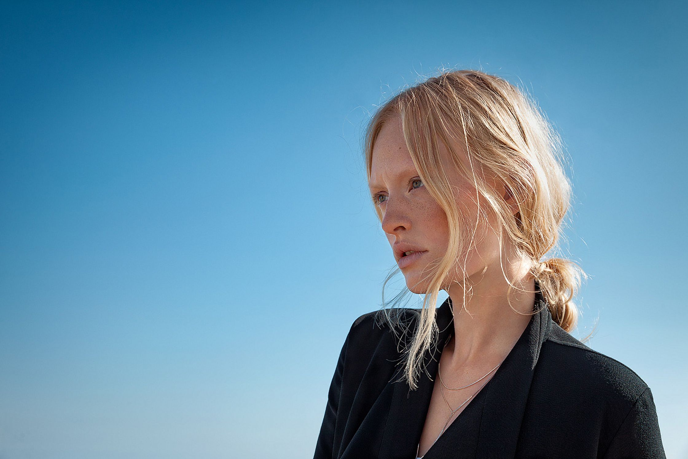 a woman in a black jacket standing in front of a blue sky  retouche advertising campaign