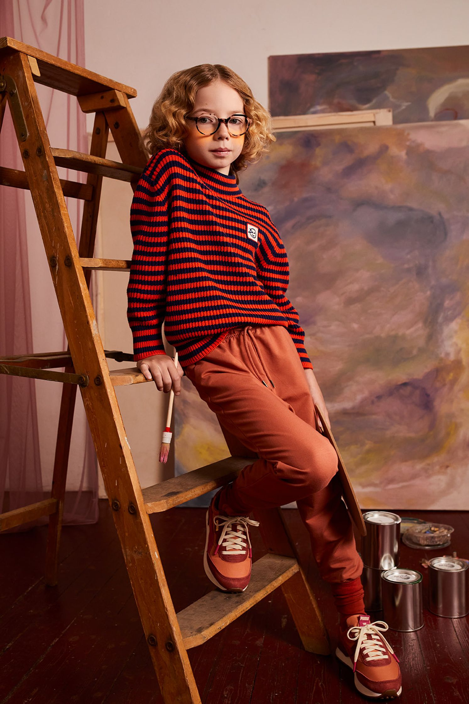 a young girl in a red striped sweater standing on a ladder in front of a painting