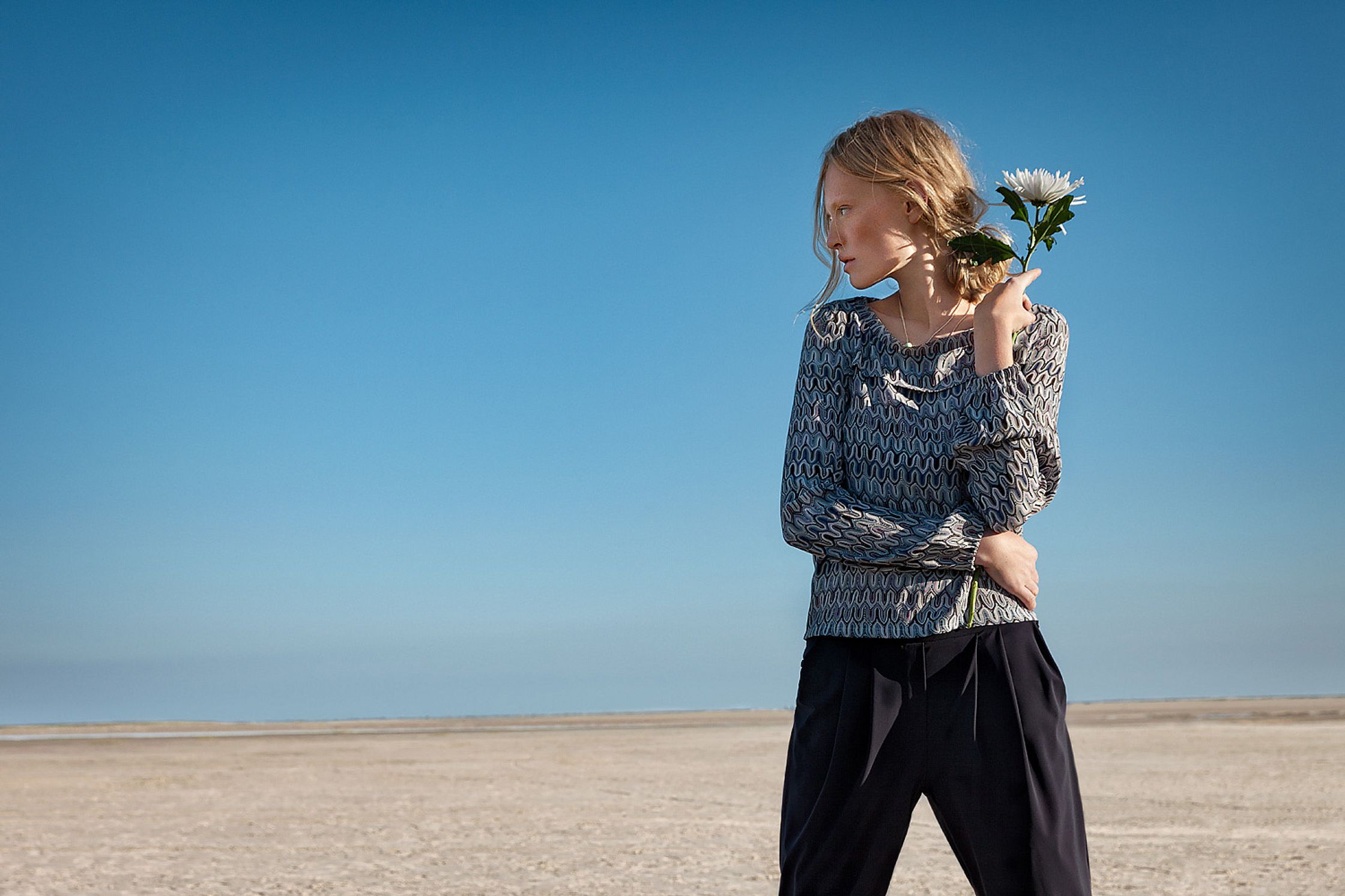 a woman standing in the desert holding a flower retouche advertising campaign