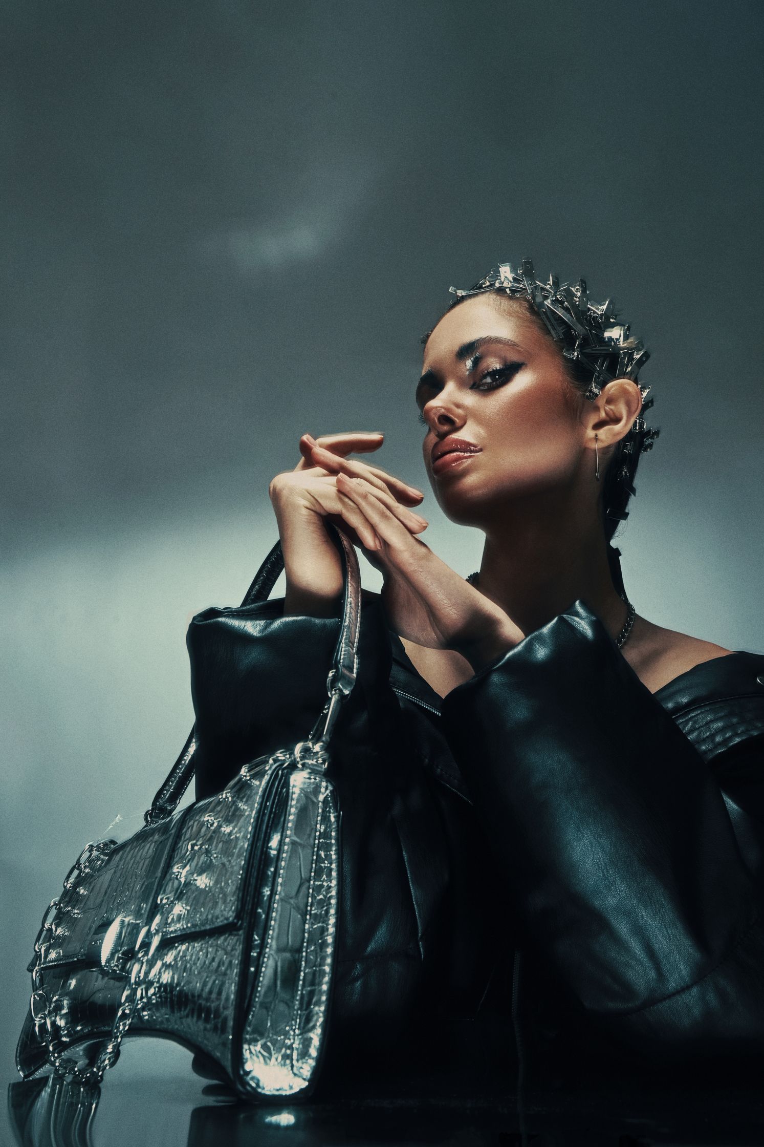 Model Monique Bourscheid posing in a black jacket with a metallic purse, creating a futuristic beauty look.