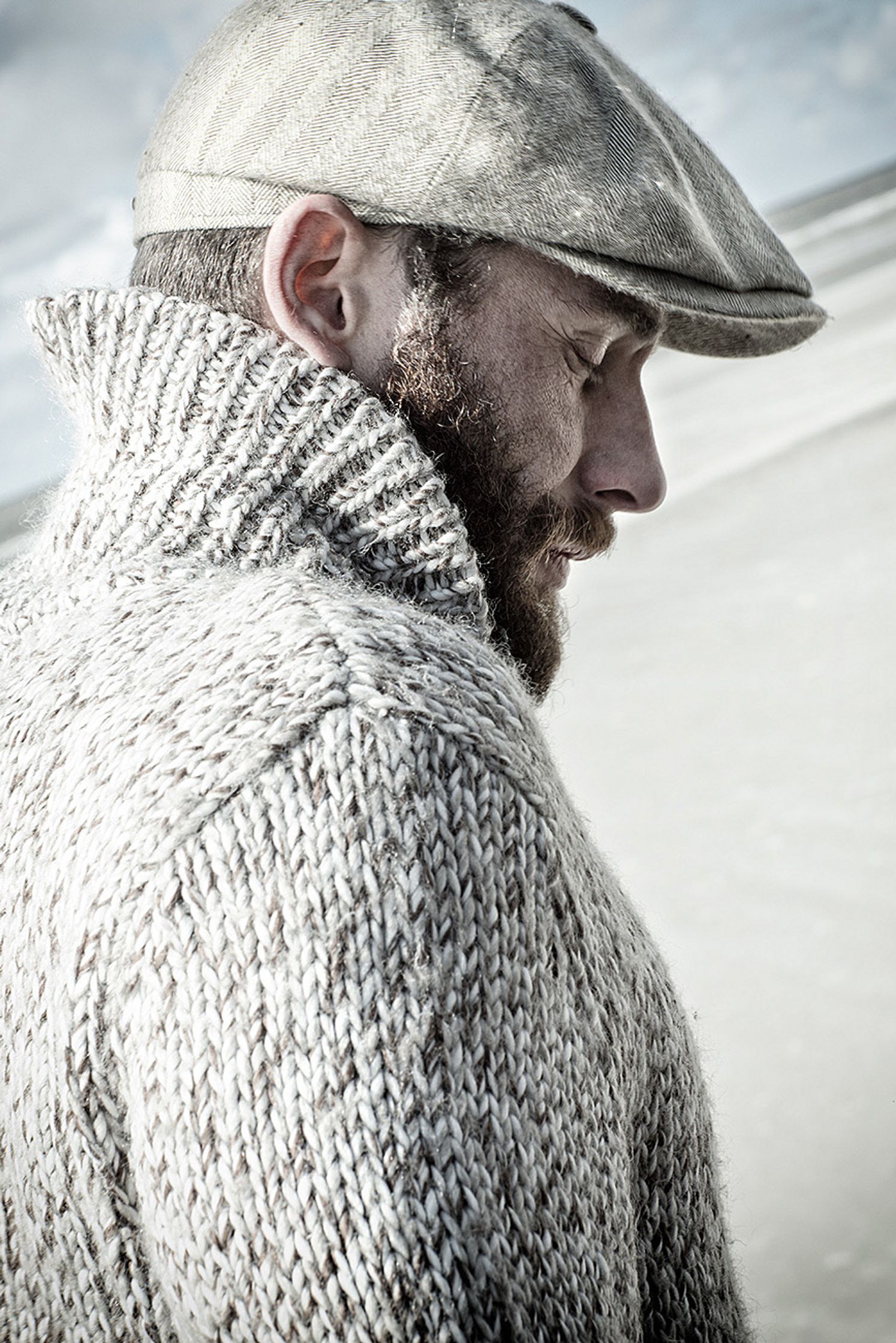 a bearded man wearing a hat and sweater on the beach Bildbearbeitung image campaign