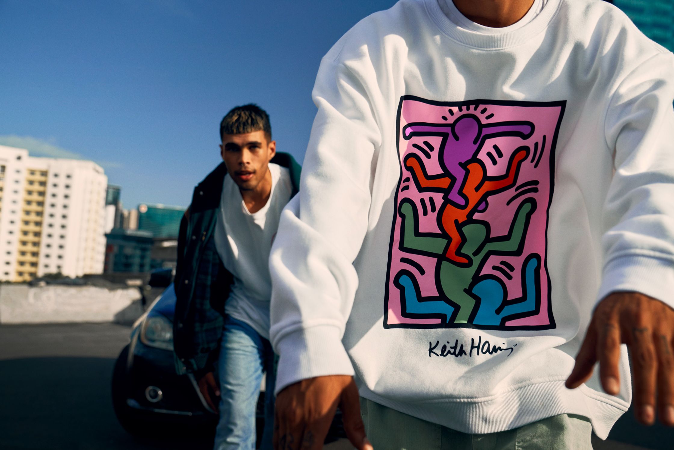 two men walking in front of a car with a colorful sweatshirt