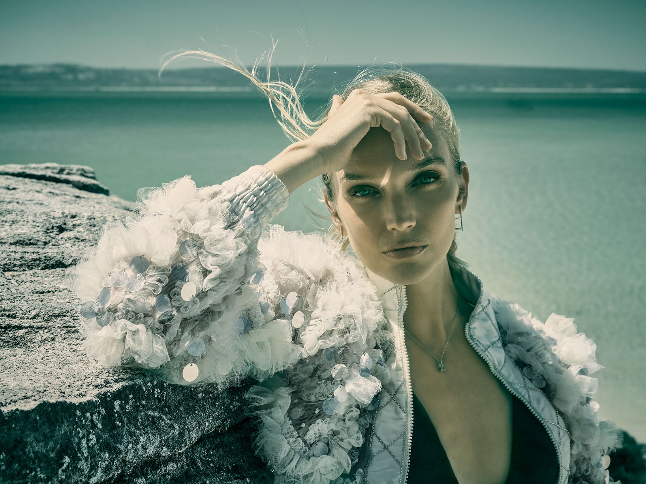 a woman is leaning against a rock by the water