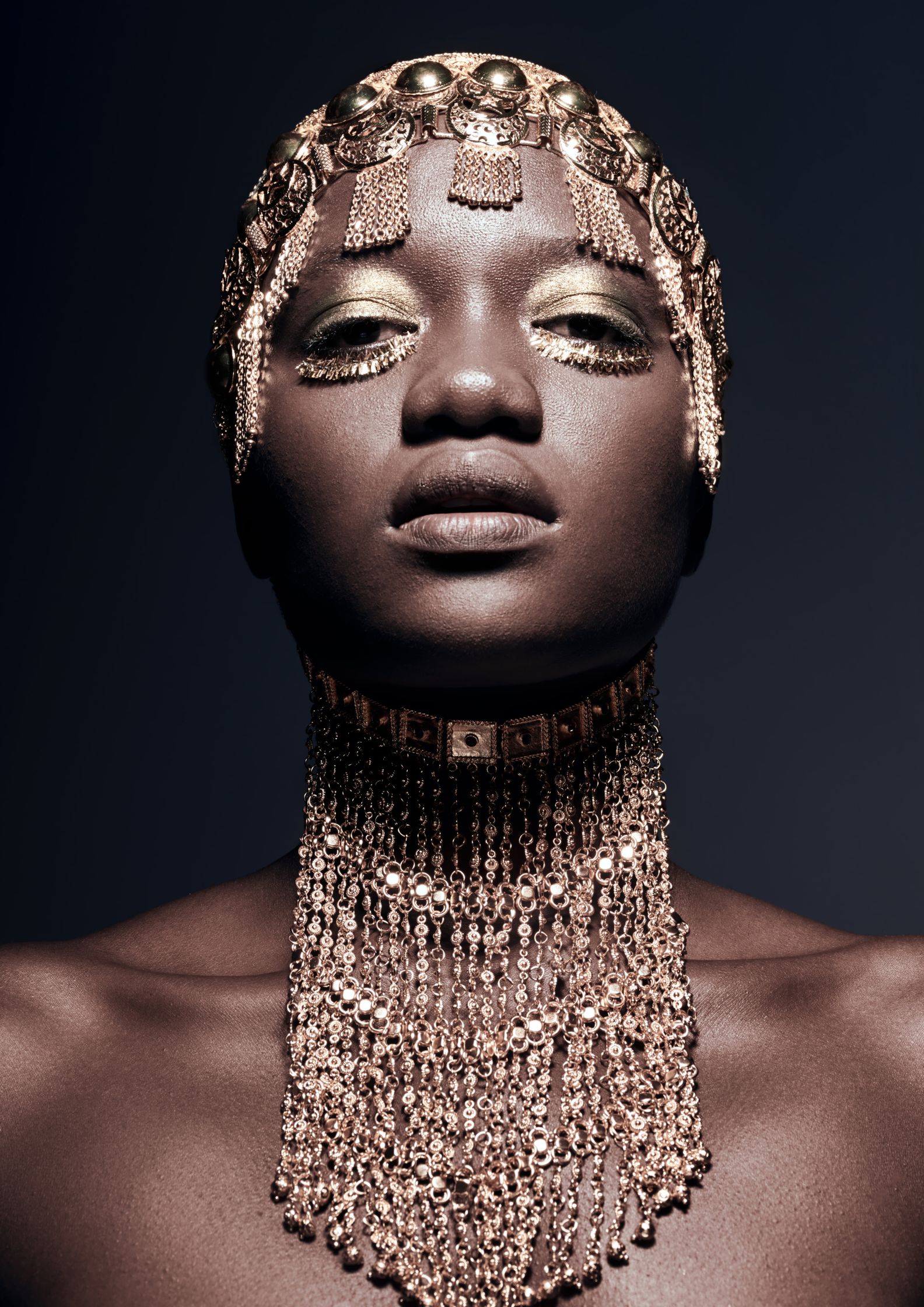 Beauty portrait featuring model with golden jewelry headpiece and metallic makeup, embodying luxury and regality