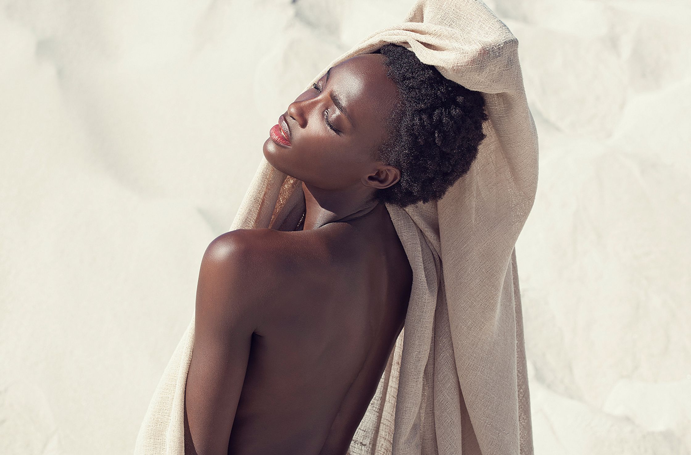 a black woman with a towel on her back posing in the sand skin retouch