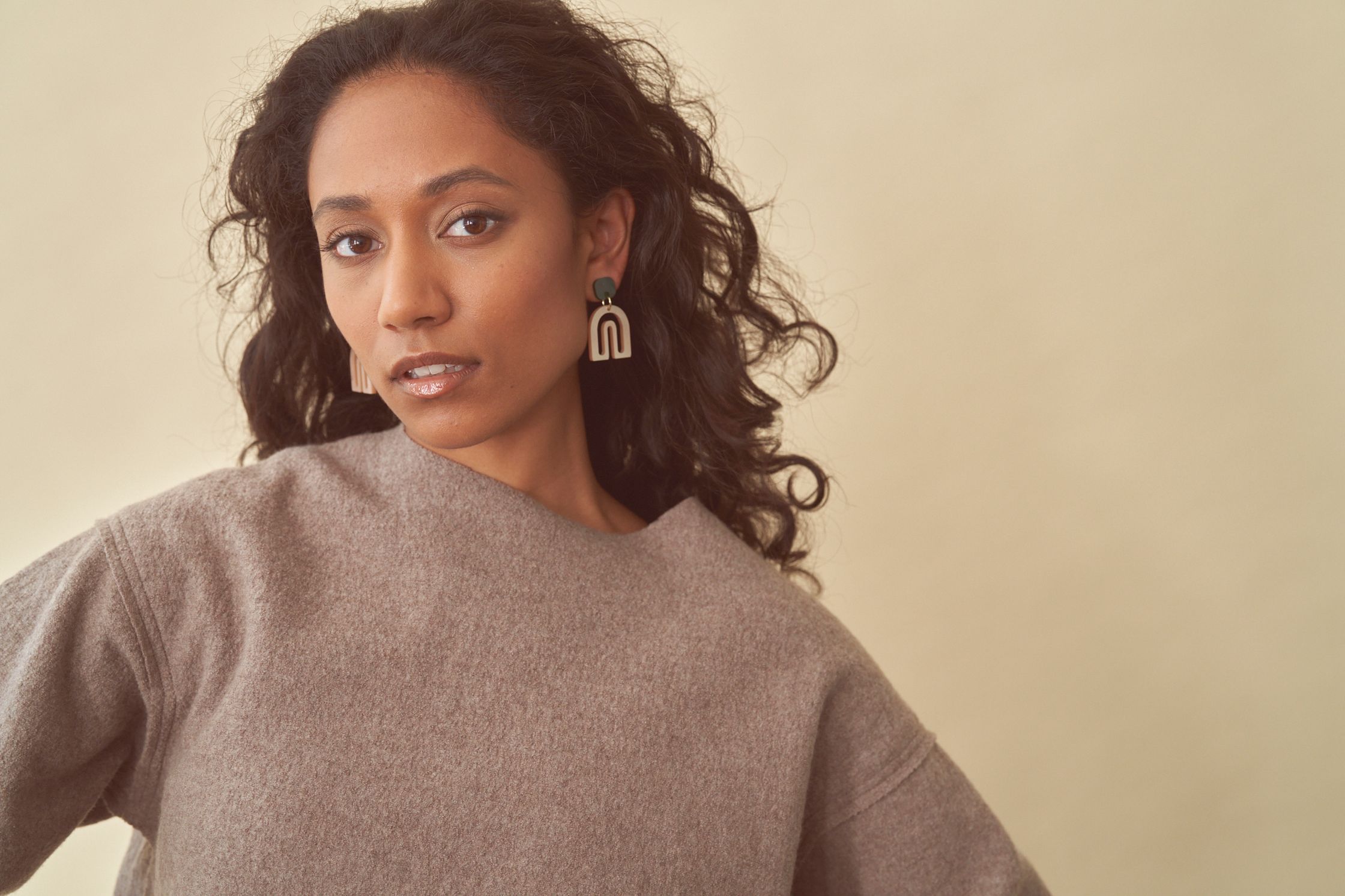 Model Devi Boddu wearing a beige sweater and green and white Vanto earrings. Hair and makeup by Denise Dedich.