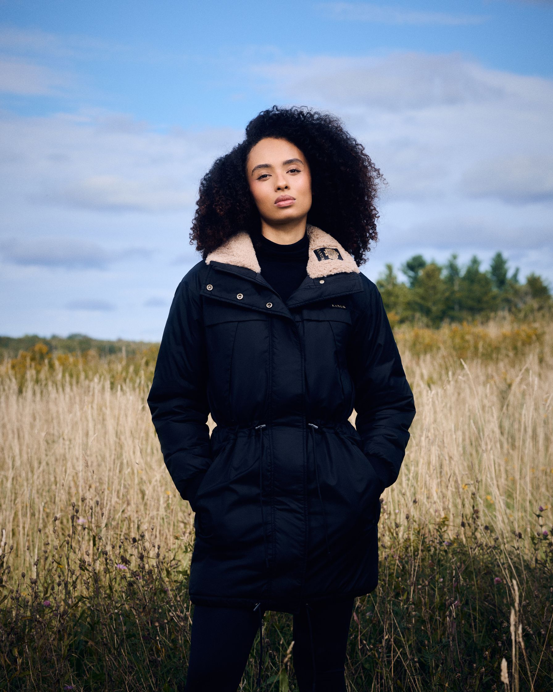 a woman in a black parka standing in a field