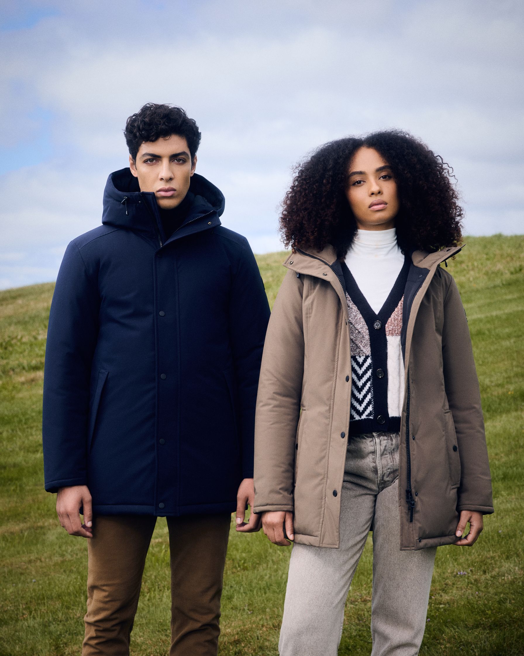 a man and woman standing in a field wearing parkas