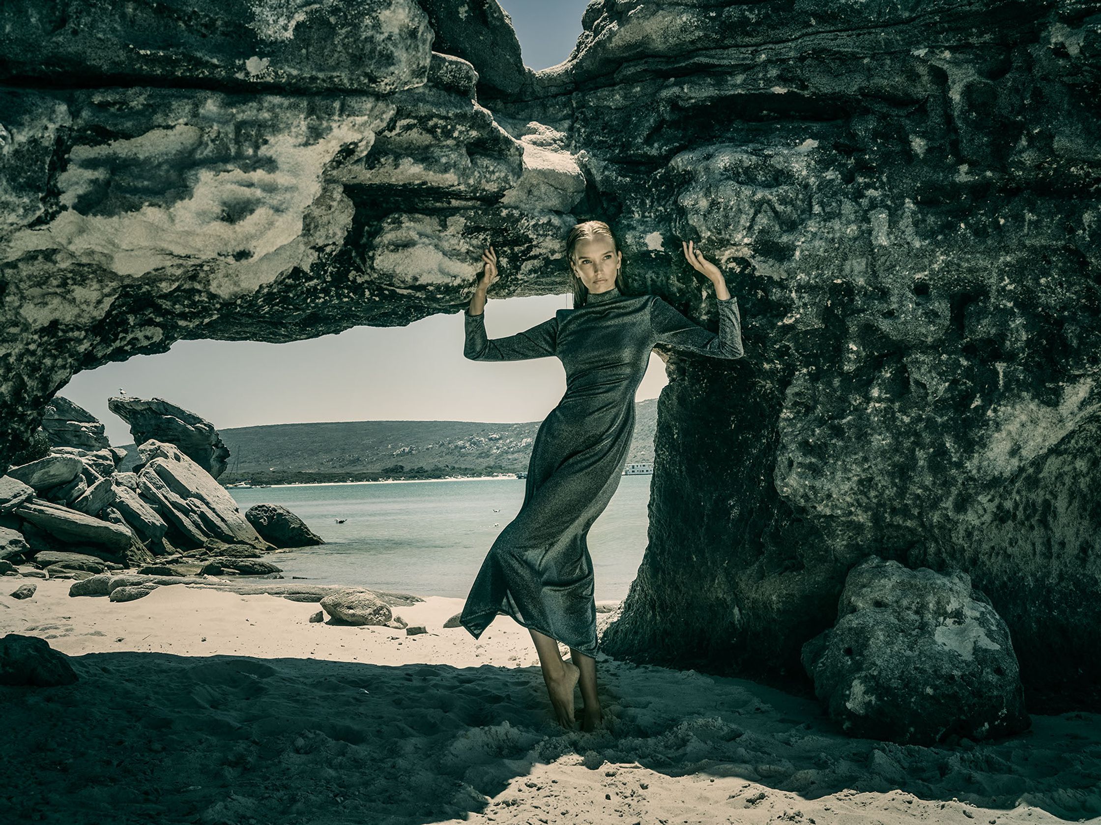 a woman posing in front of a large rock