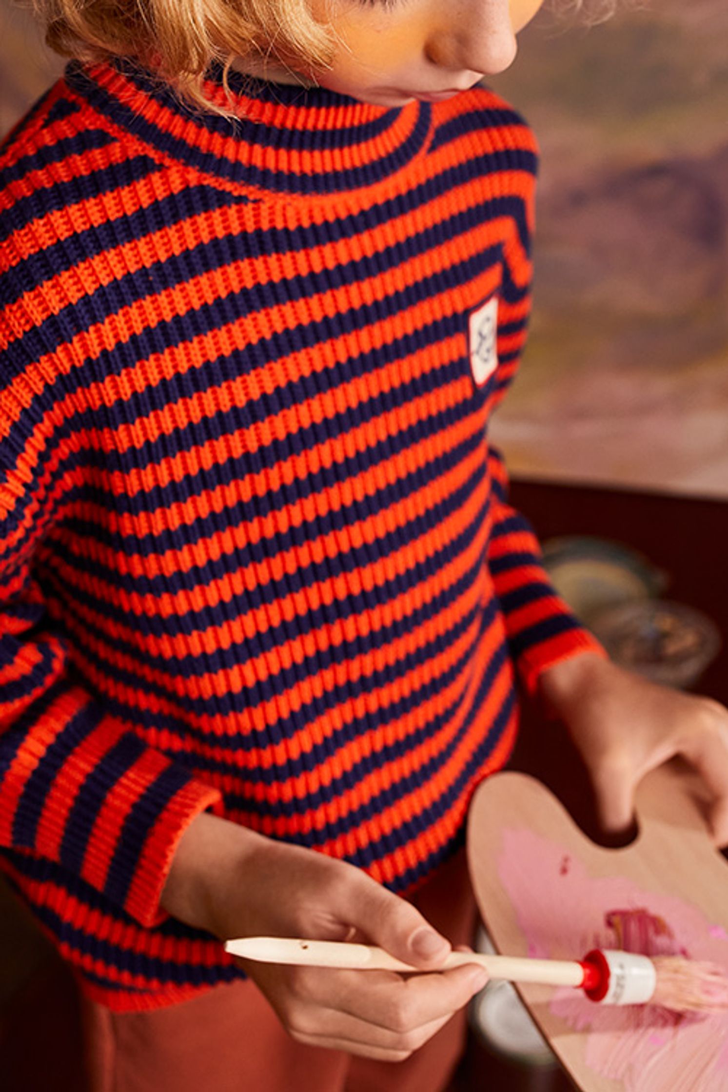 a child wearing a red and blue striped sweater holding a paint brush