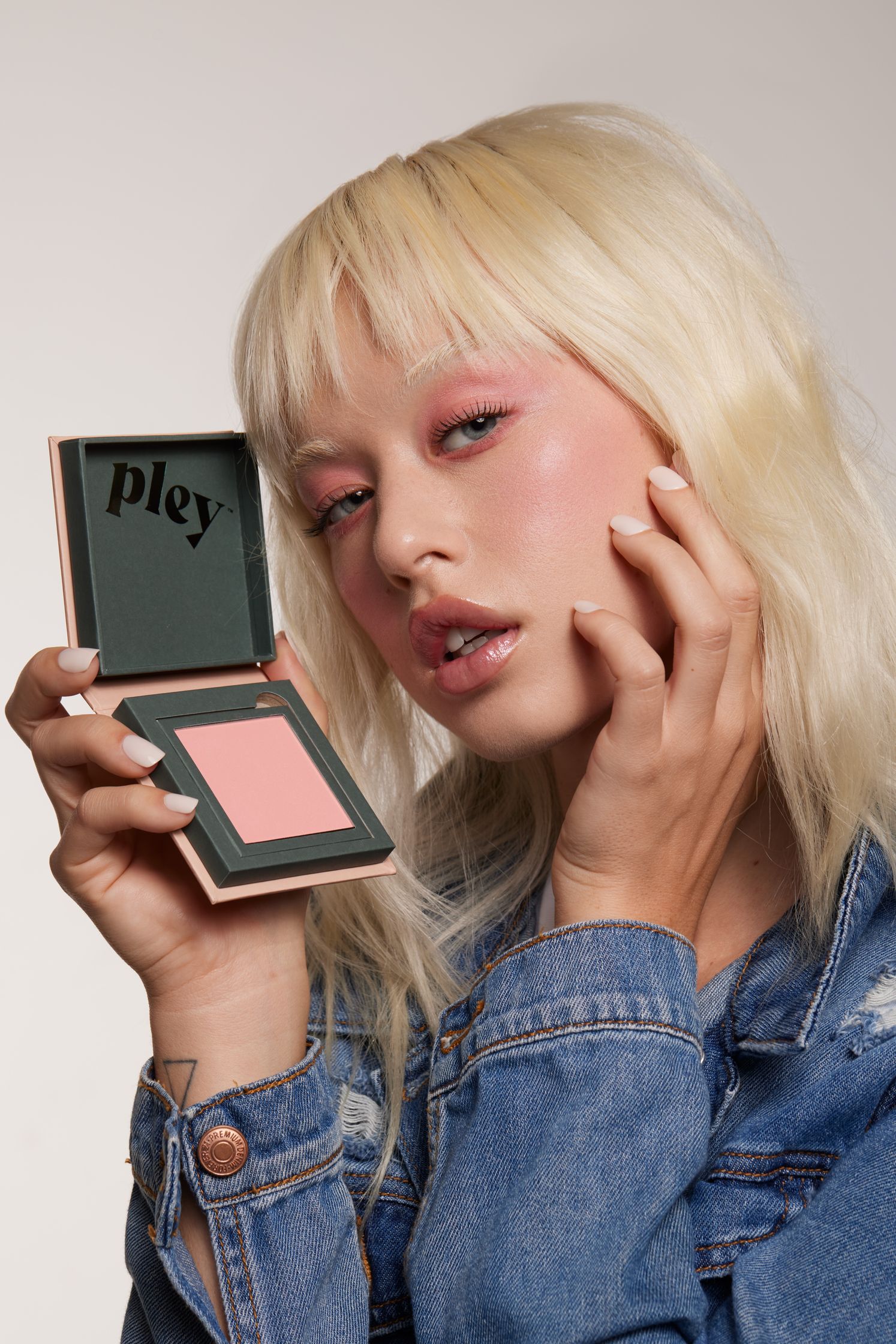 a blonde woman holding a pink blush compact