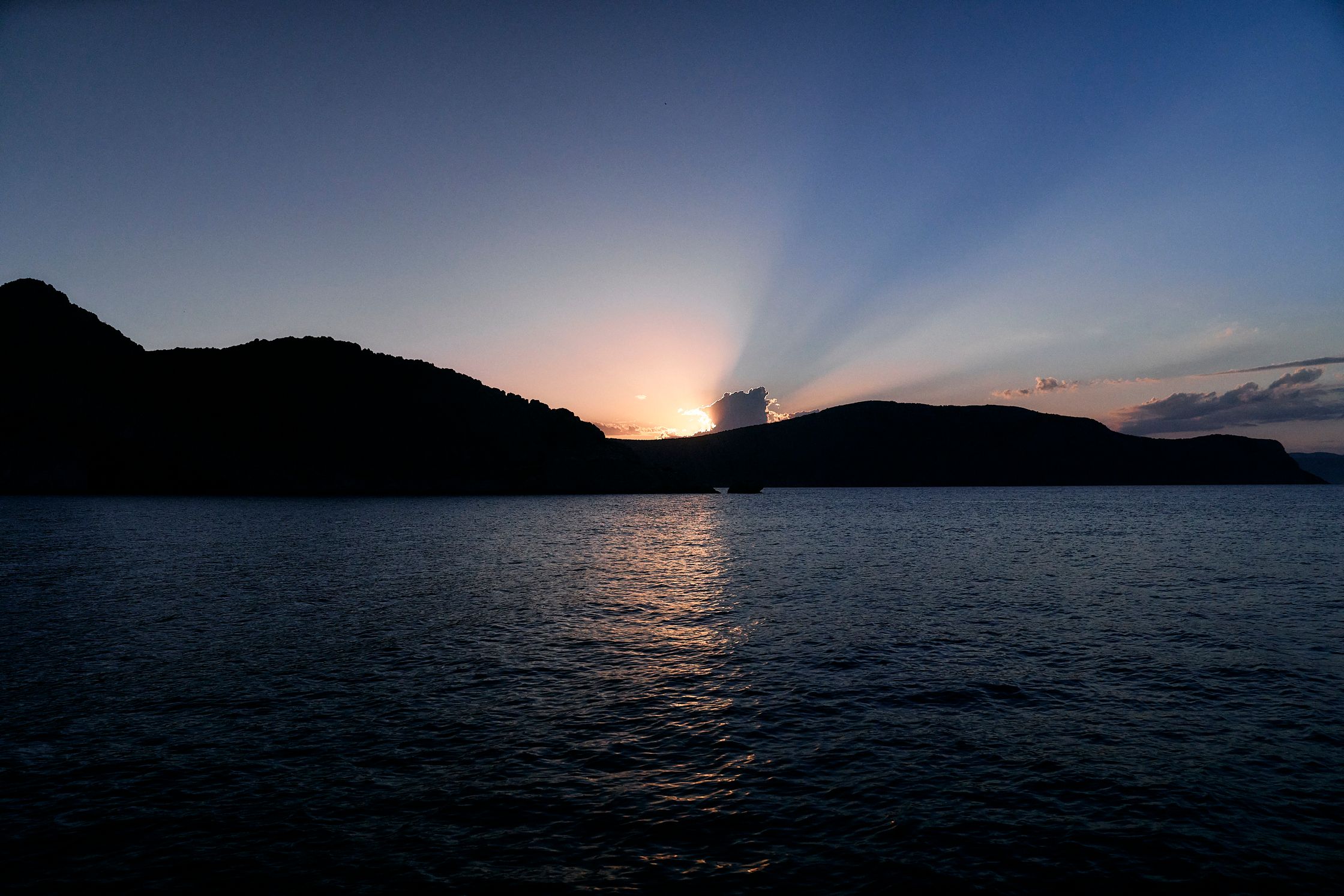 the sun is setting over a body of water with mountains in the background