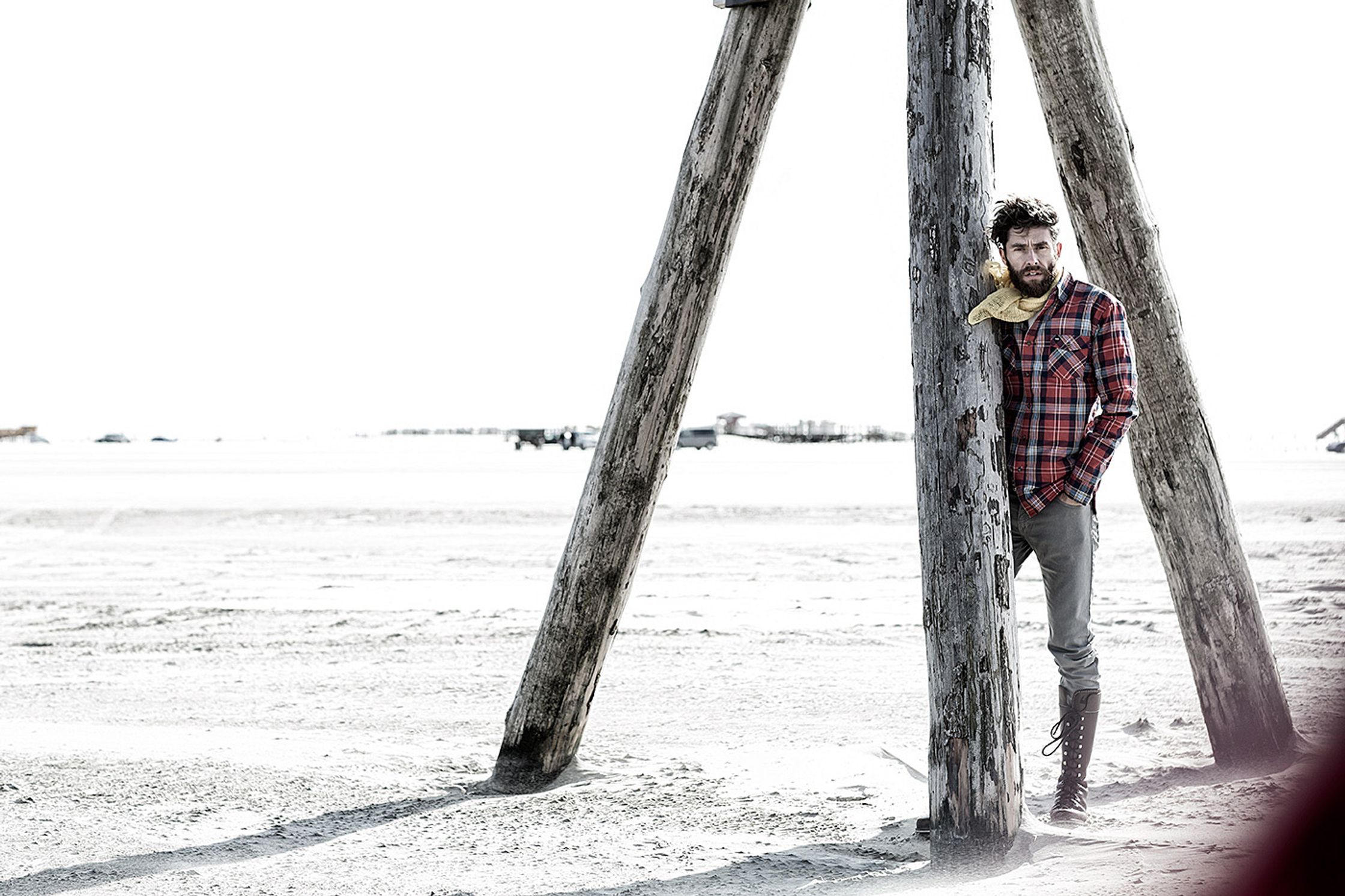 a man leaning against a wooden pole on the beach post production image campaign