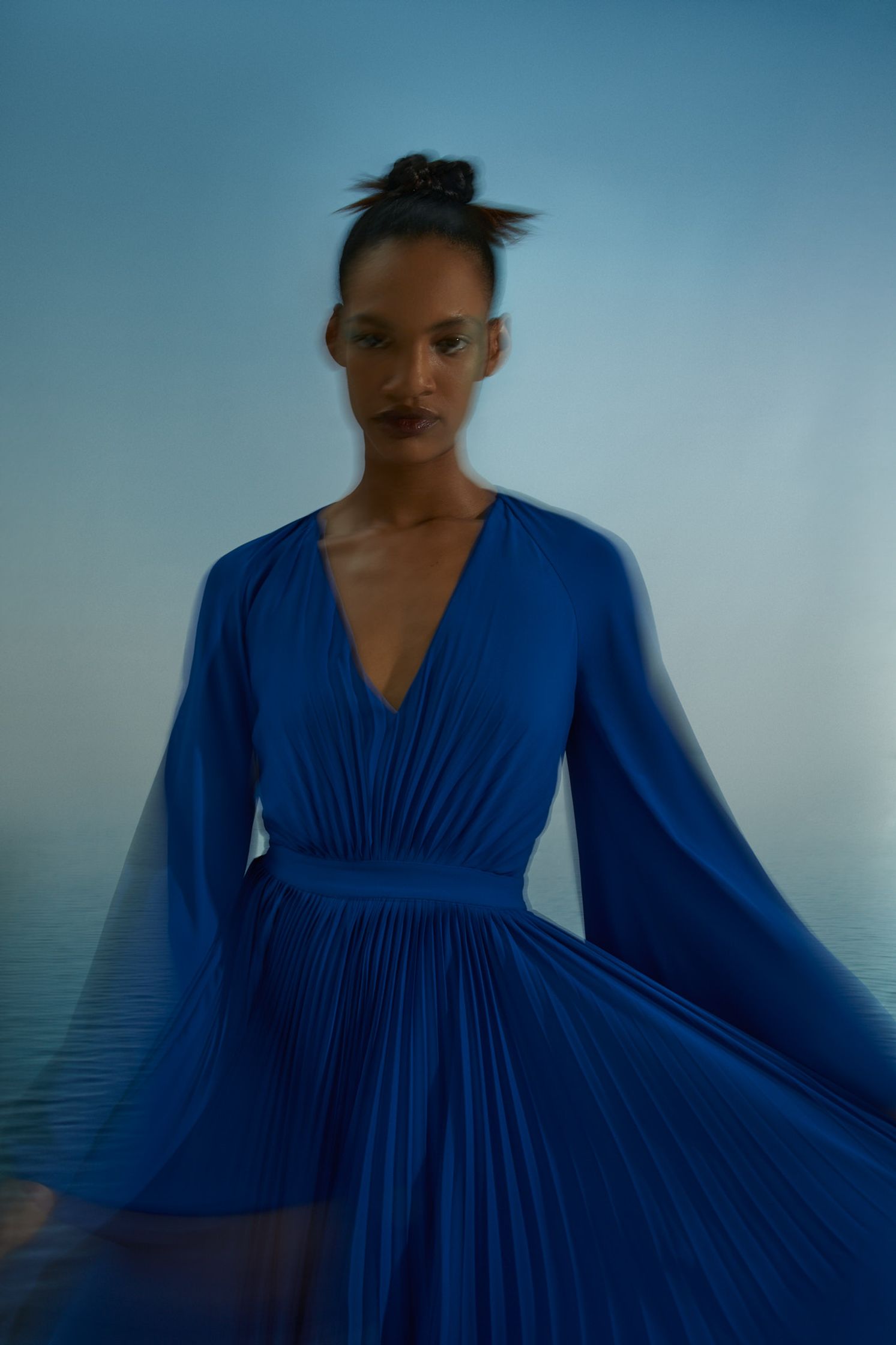 a woman in a blue dress standing by the ocean