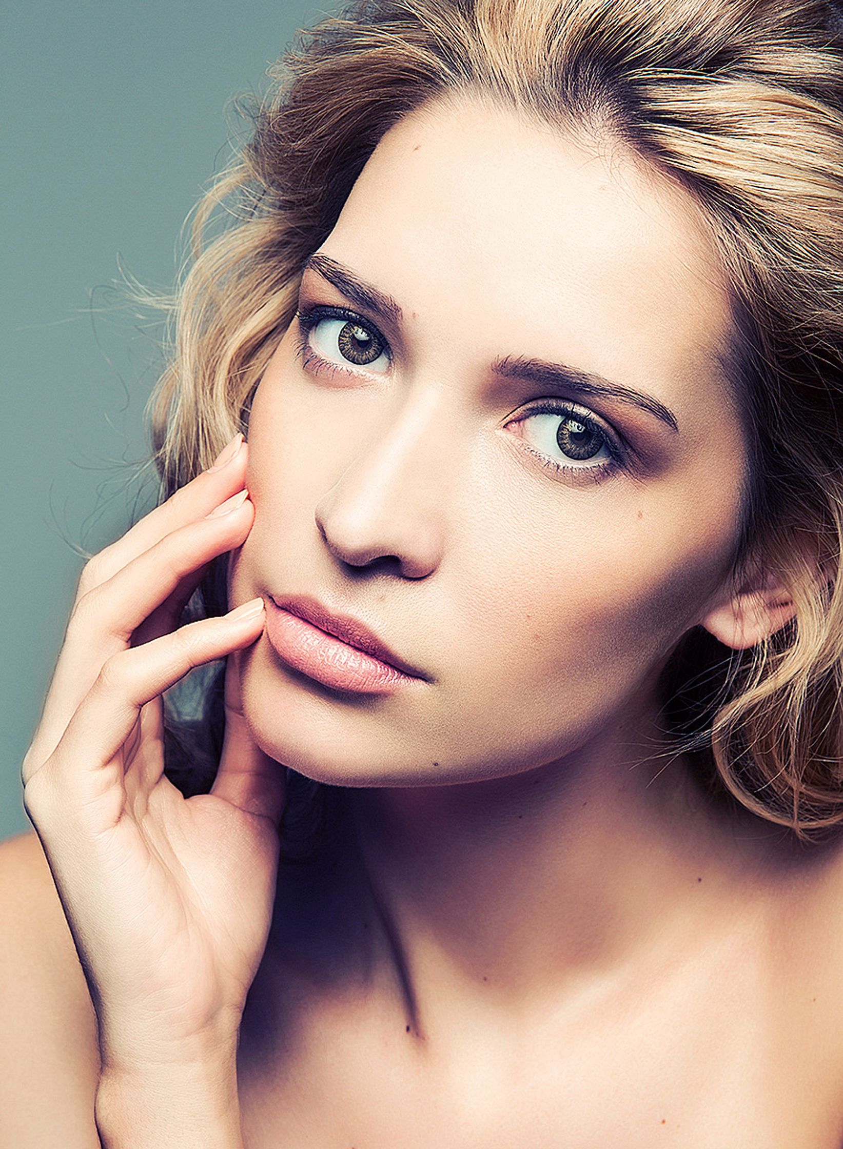 a blond woman posing with her hand on her face beauty post production