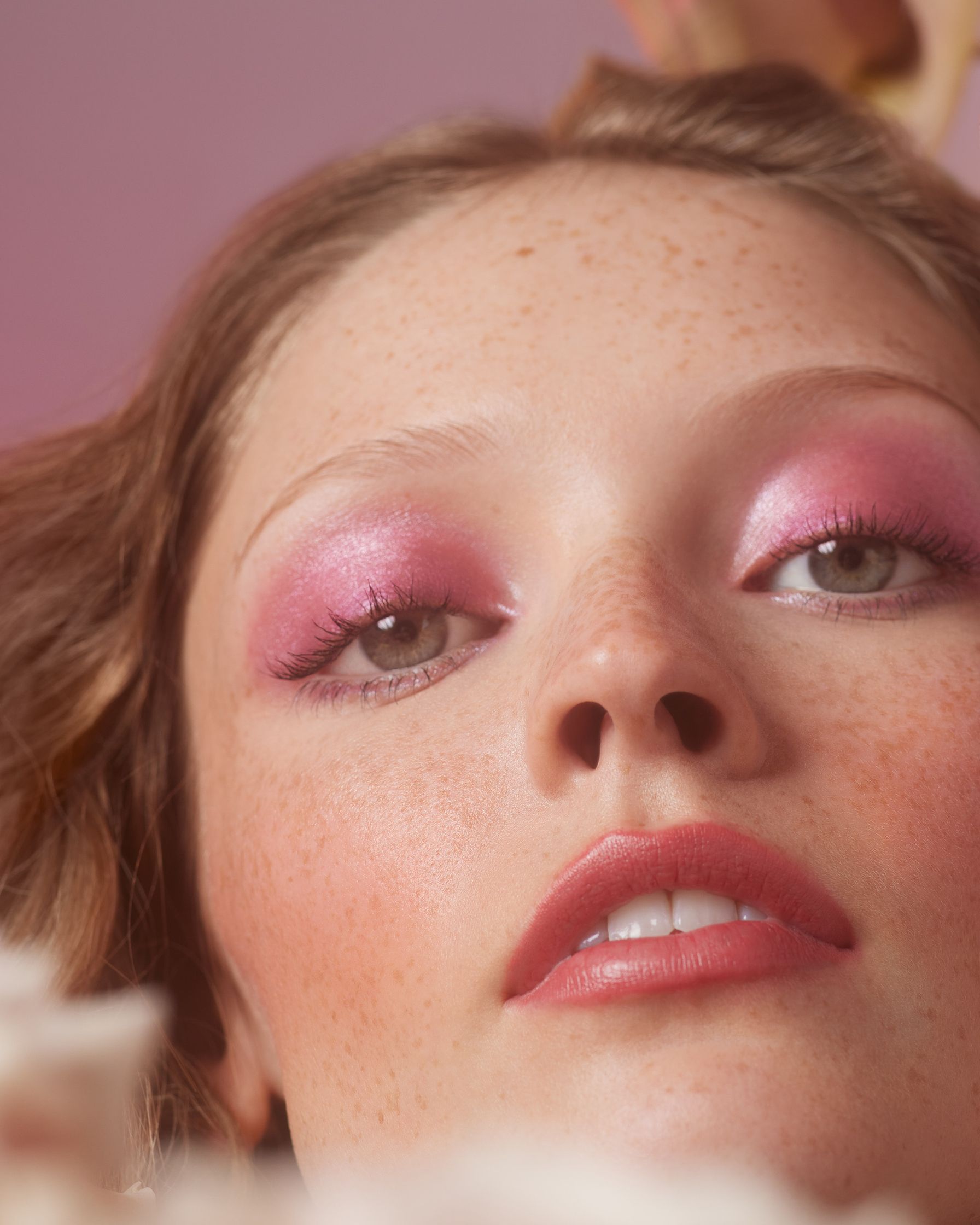 a woman with pink eye makeup laying on a pink flower